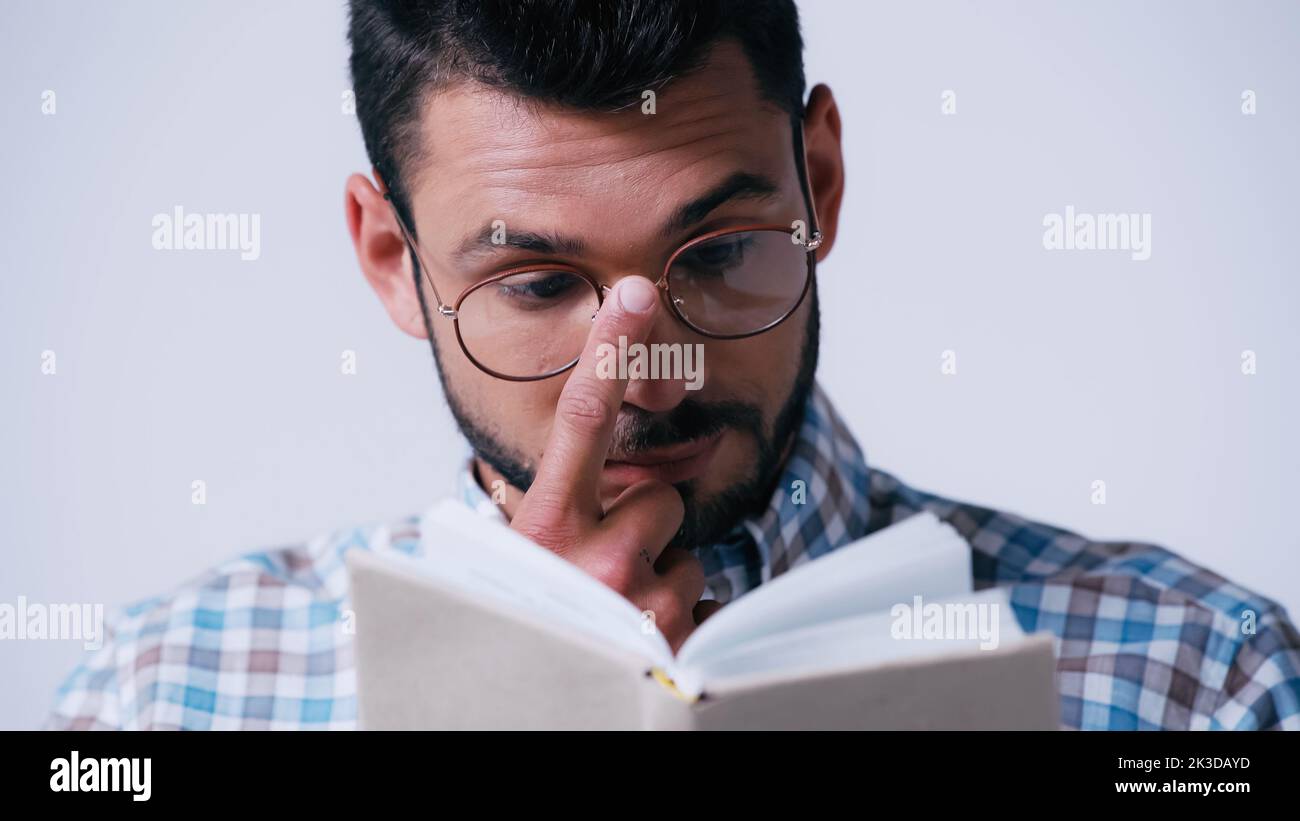 nerd étudiant ajustement de lunettes tout en lisant livre flou isolé sur gris, image de stock Banque D'Images