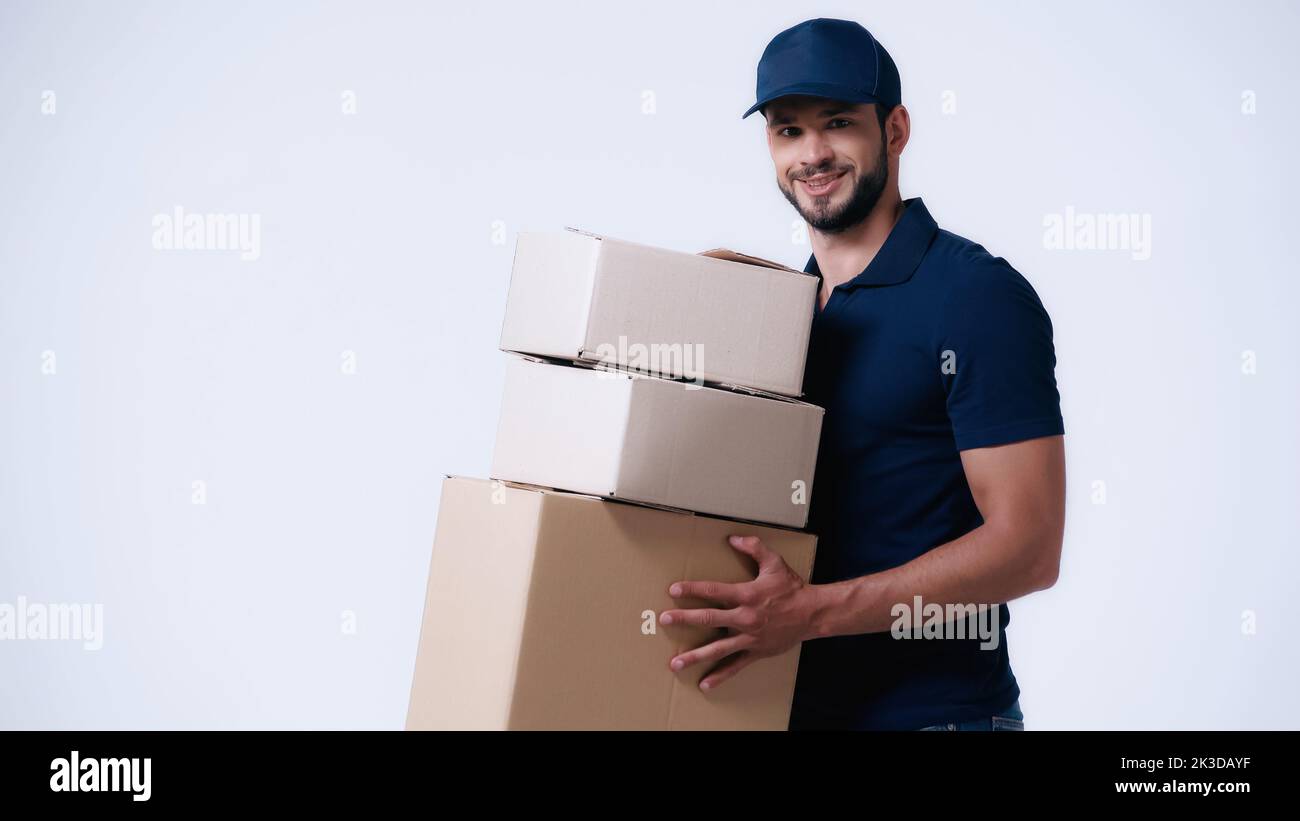 liveur souriant transportant des boîtes en carton isolées sur blanc, image de stock Banque D'Images