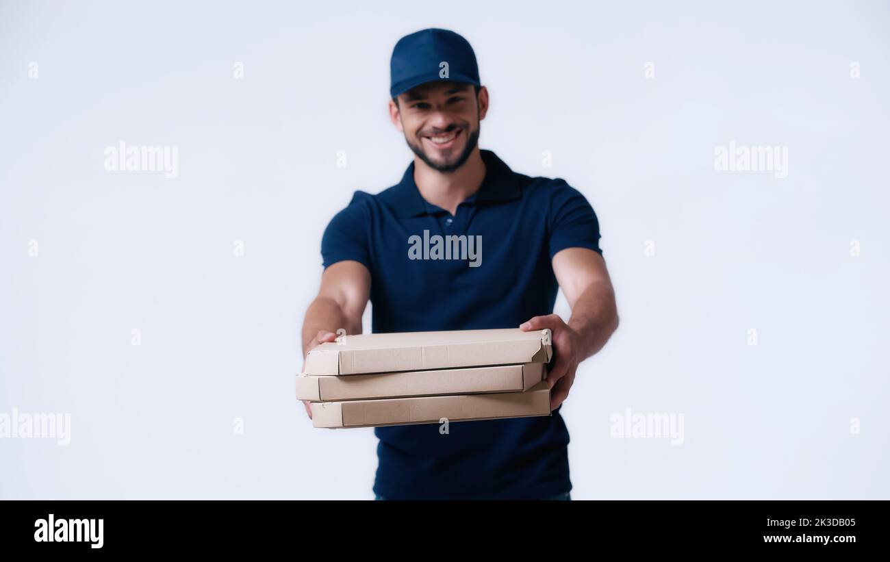 joyeux livreur donnant des boîtes de pizza tout en regardant la caméra isolée sur blanc, image de stock Banque D'Images