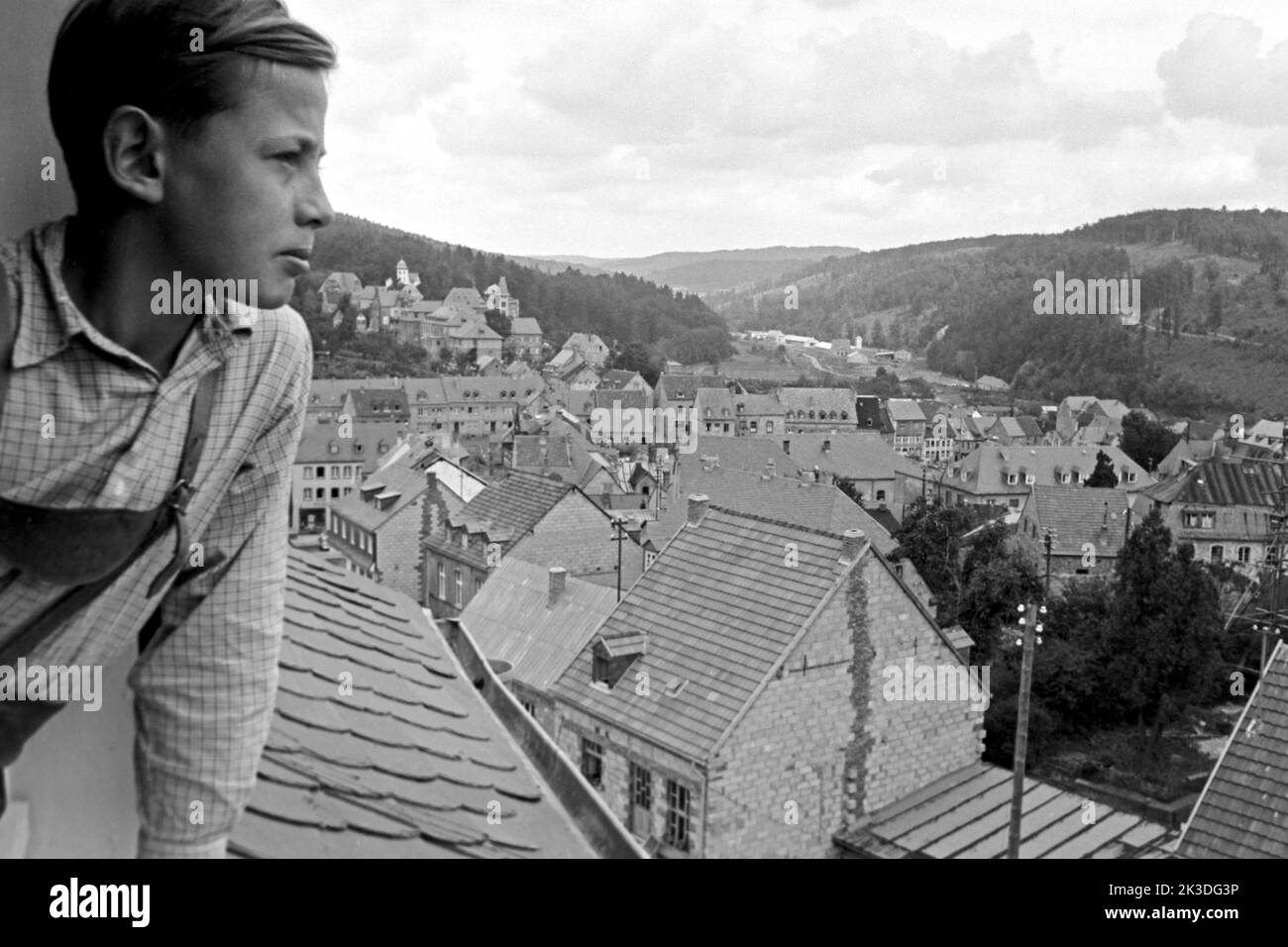 Junge im Fenster blickt über Prüm in der Eifel, vers 1952. Garçon regardant par une fenêtre sur Prüm, région d'Eifel, vers 1952. Banque D'Images