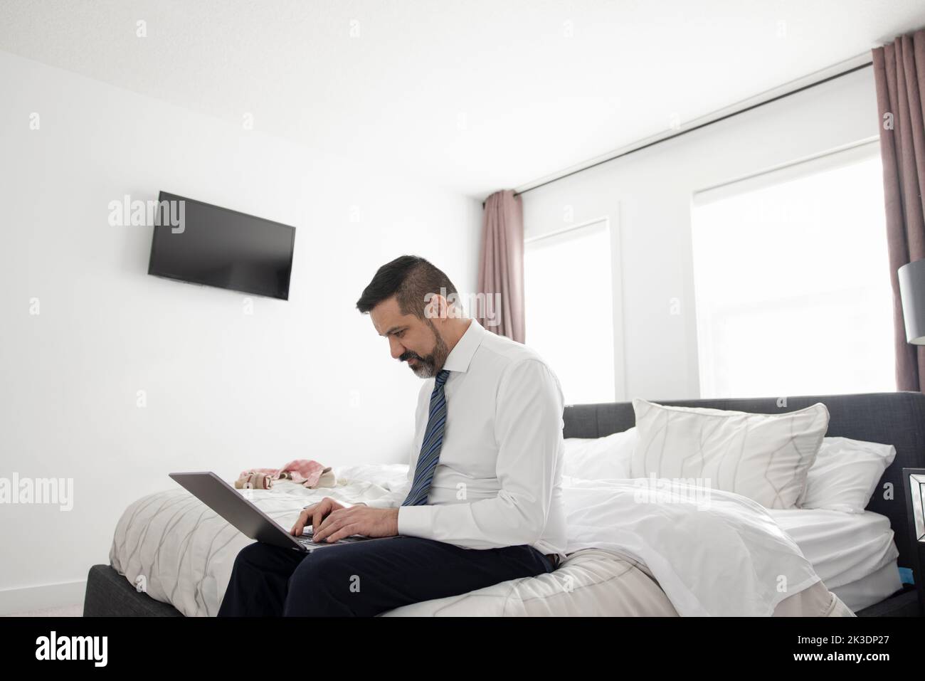 homme d'affaires en chemise et cravate travaillant à un ordinateur portable sur le lit Banque D'Images