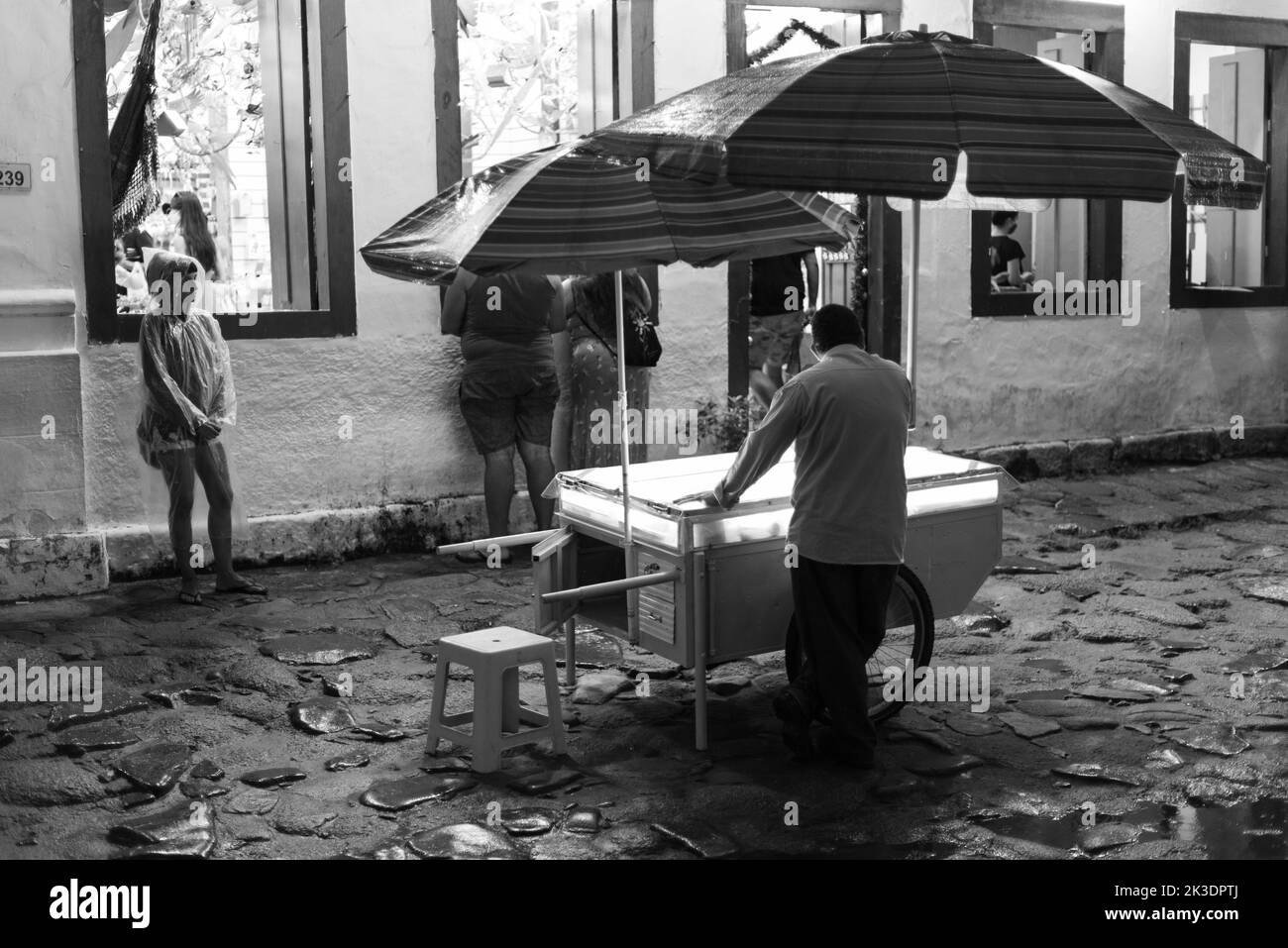 Une photo en niveaux de gris d'un vendeur de crème glacée lors d'une nuit de pluie à Paraty, Brésil Banque D'Images