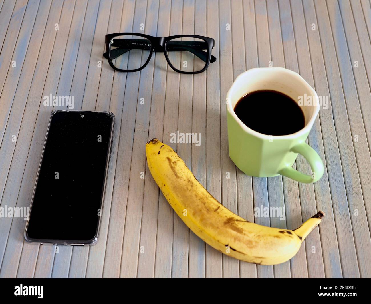 Gros plan d'une tasse de café, d'une banane, d'un smartphone et de verres sur une table en bois Banque D'Images