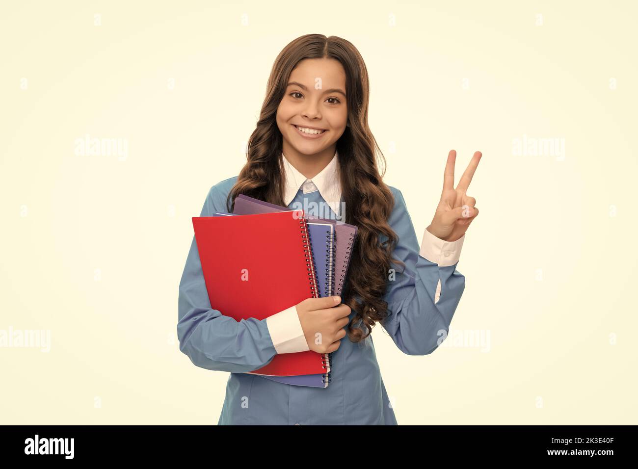 portrait d'enfant heureux avec cahier d'école isolé sur le geste de paix de spectacle blanc, lycée. Banque D'Images