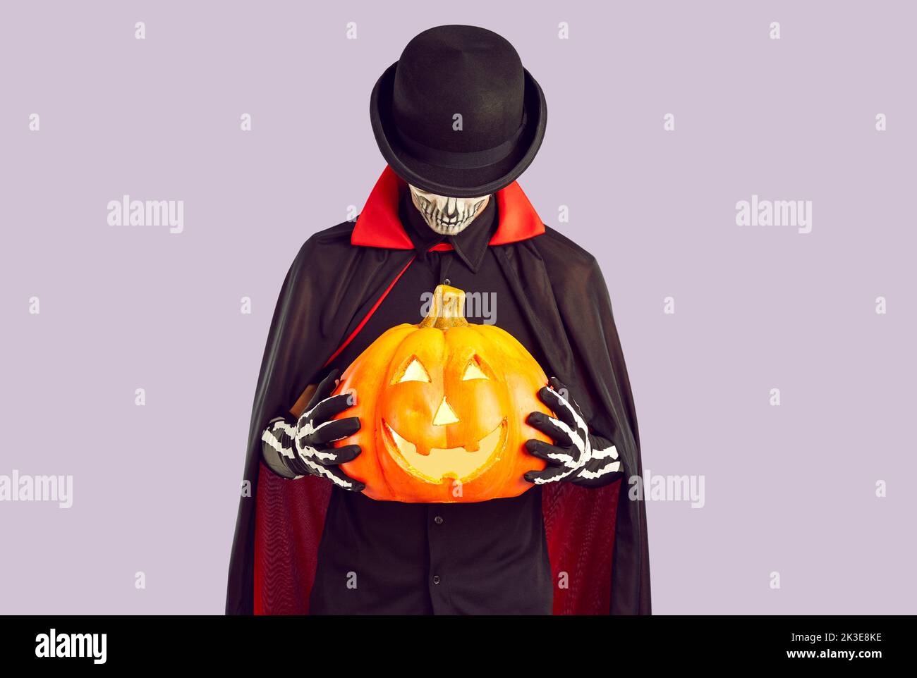 Homme vêtu d'un chapeau noir, d'un manteau et de gants de squelette tenant une citrouille d'Halloween Banque D'Images