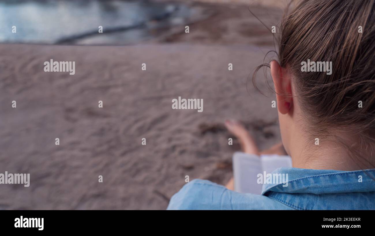 Foyer sélectif d'une femme assise avec son dos à la caméra et lisant un livre sur la plage Banque D'Images