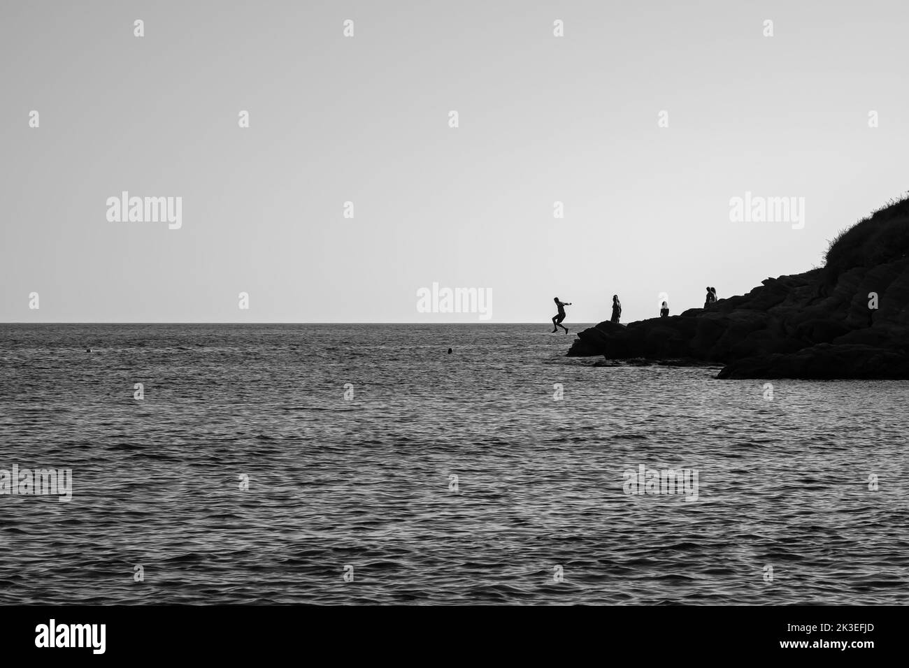 Touristes sautant une falaise à la plage de Mylopotas à iOS Grèce en noir et blanc Banque D'Images
