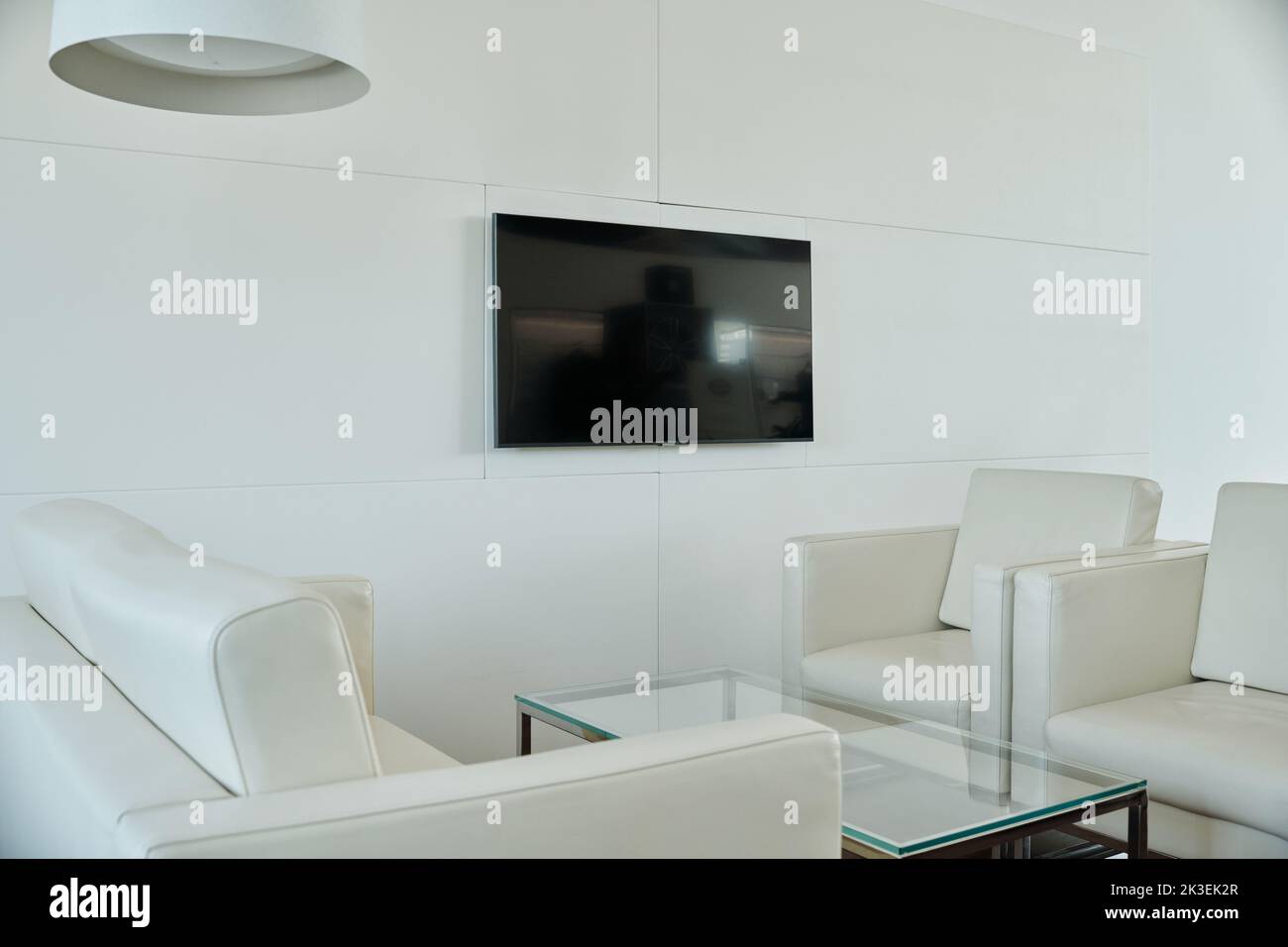 Canapé en cuir blanc et deux fauteuils entourant une table rectangulaire en verre debout au mur avec écran de télévision noir dans un bureau à espace ouvert Banque D'Images