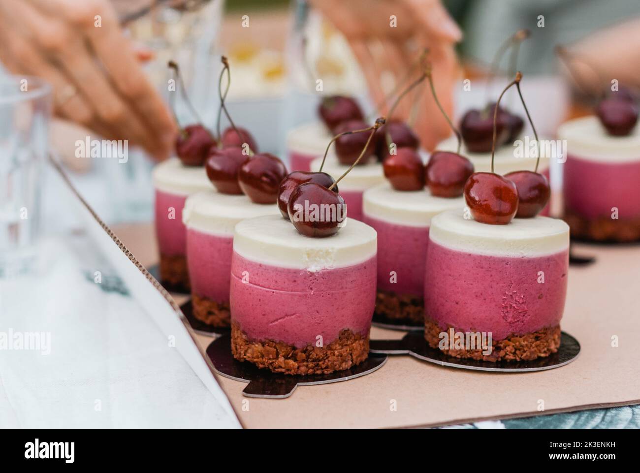 Délicieux petits gâteaux roses avec glaçage blanc et cerise rouge sur le dessus avec une base de chocolat. Banque D'Images