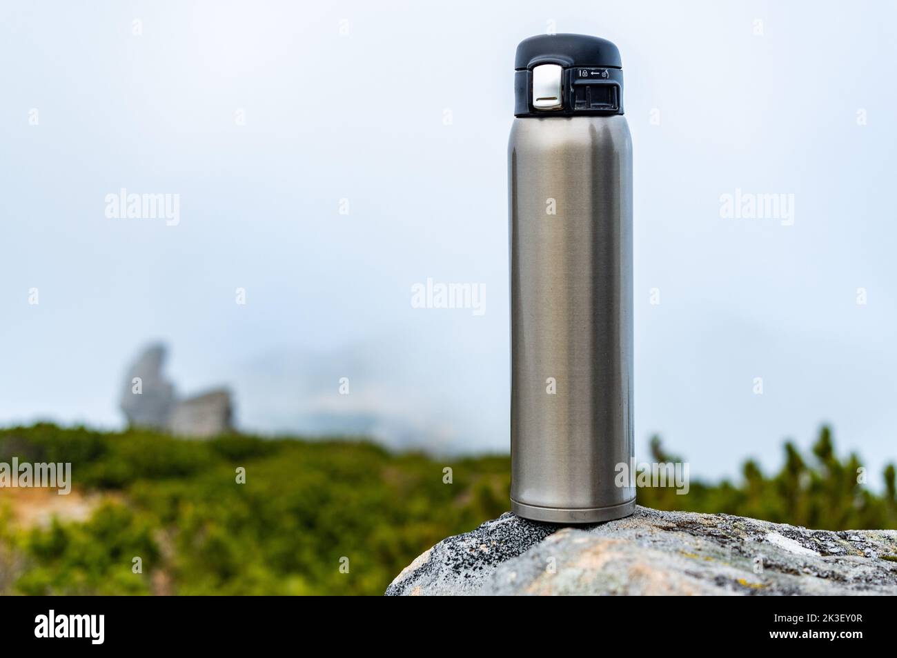 Thermos en acier sur une pierre. Bouteille en acier sur une pierre dans les montagnes. Bouteille sur le fond des nuages et des montagnes. Vue avant. Banque D'Images