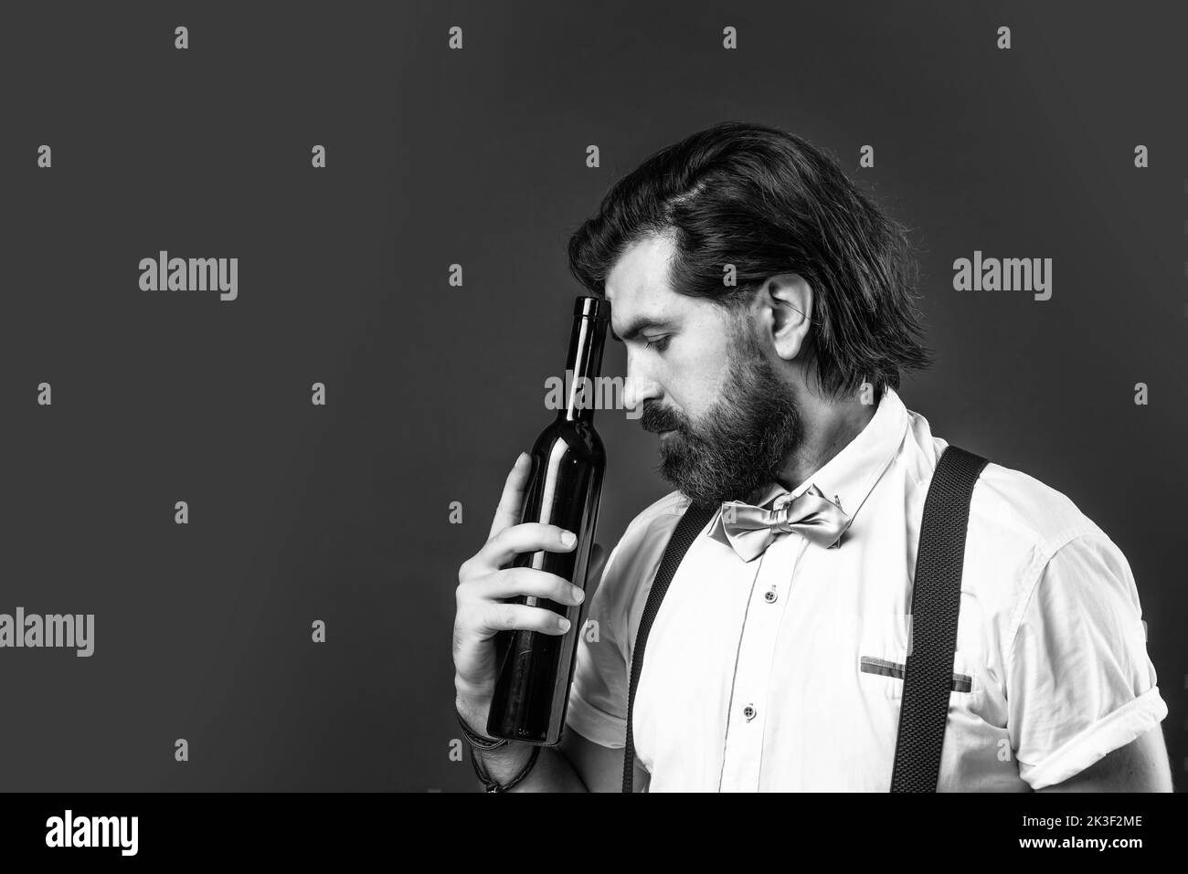 beau homme riche barbu avec moustache à cheveux et barbe en bretelles tenant une bouteille de vin, sommelier Banque D'Images