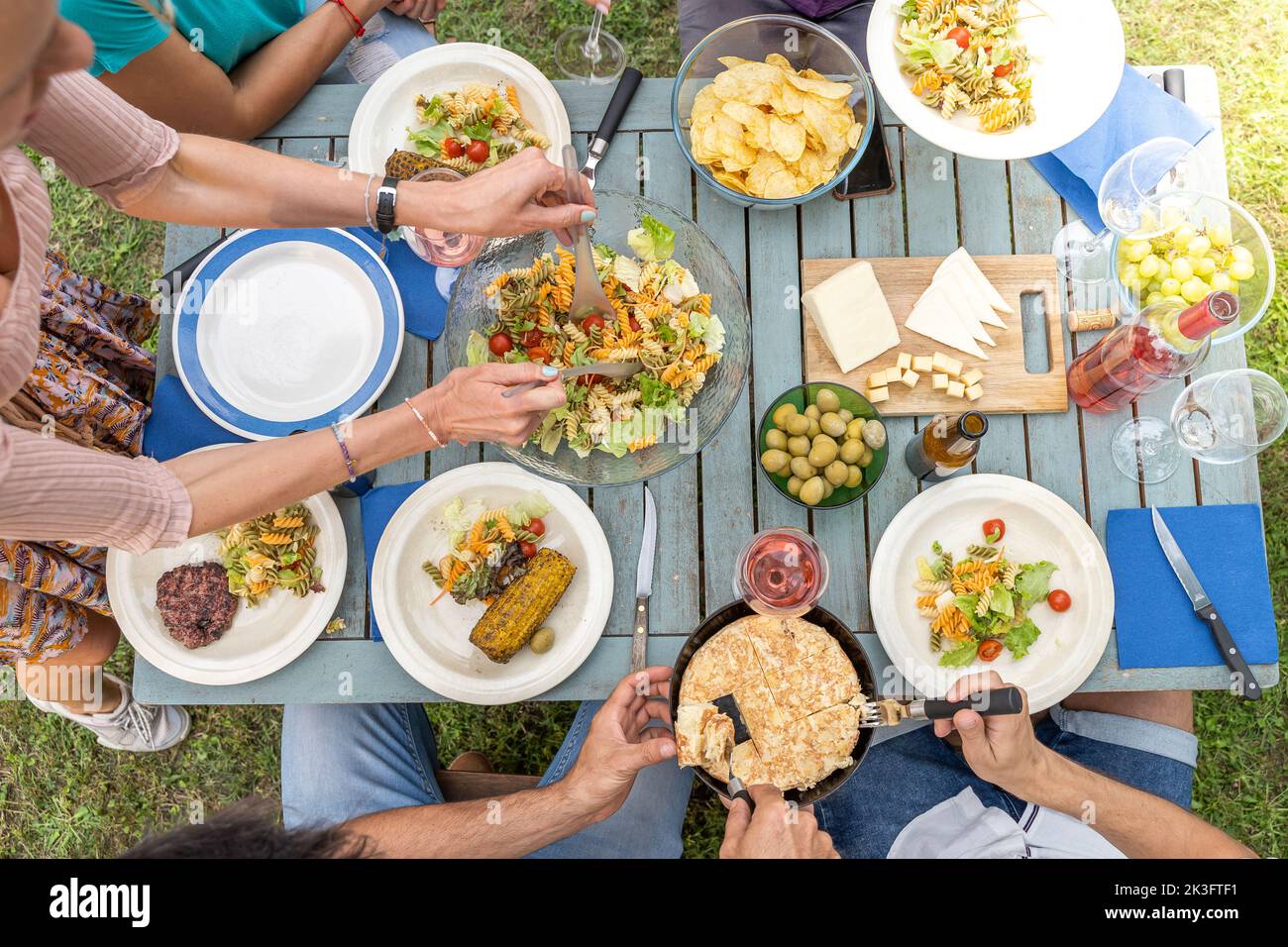 Famille multiculturelle assise à une table en bois pour dîner. Ils ont des assiettes pleines de nourriture et des verres avec des boissons. Banque D'Images