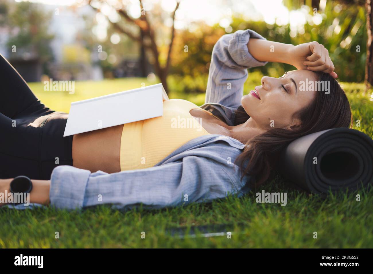 Femme sportive dormant dans le parc après une séance d'entraînement dure le matin, tenant un livre sur sa poitrine. Quarantaine à domicile. Faire du yoga et lire le livre Banque D'Images