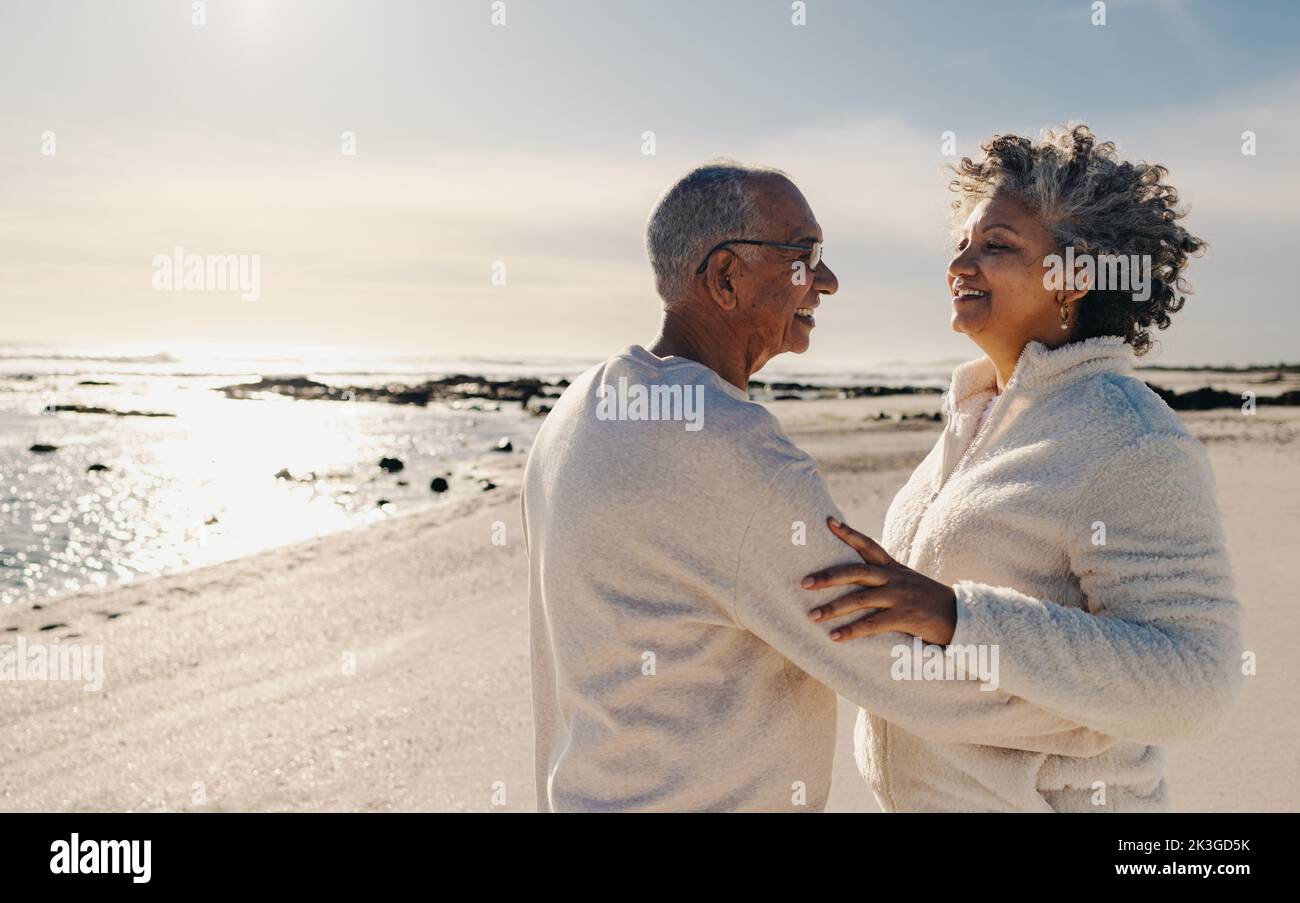 Couple d'âge mûr souriant et dansant ensemble sur le sable de la plage. Couple de personnes âgées heureux ayant un bon moment à côté de l'océan. Couple senior joyeux appréciant t Banque D'Images