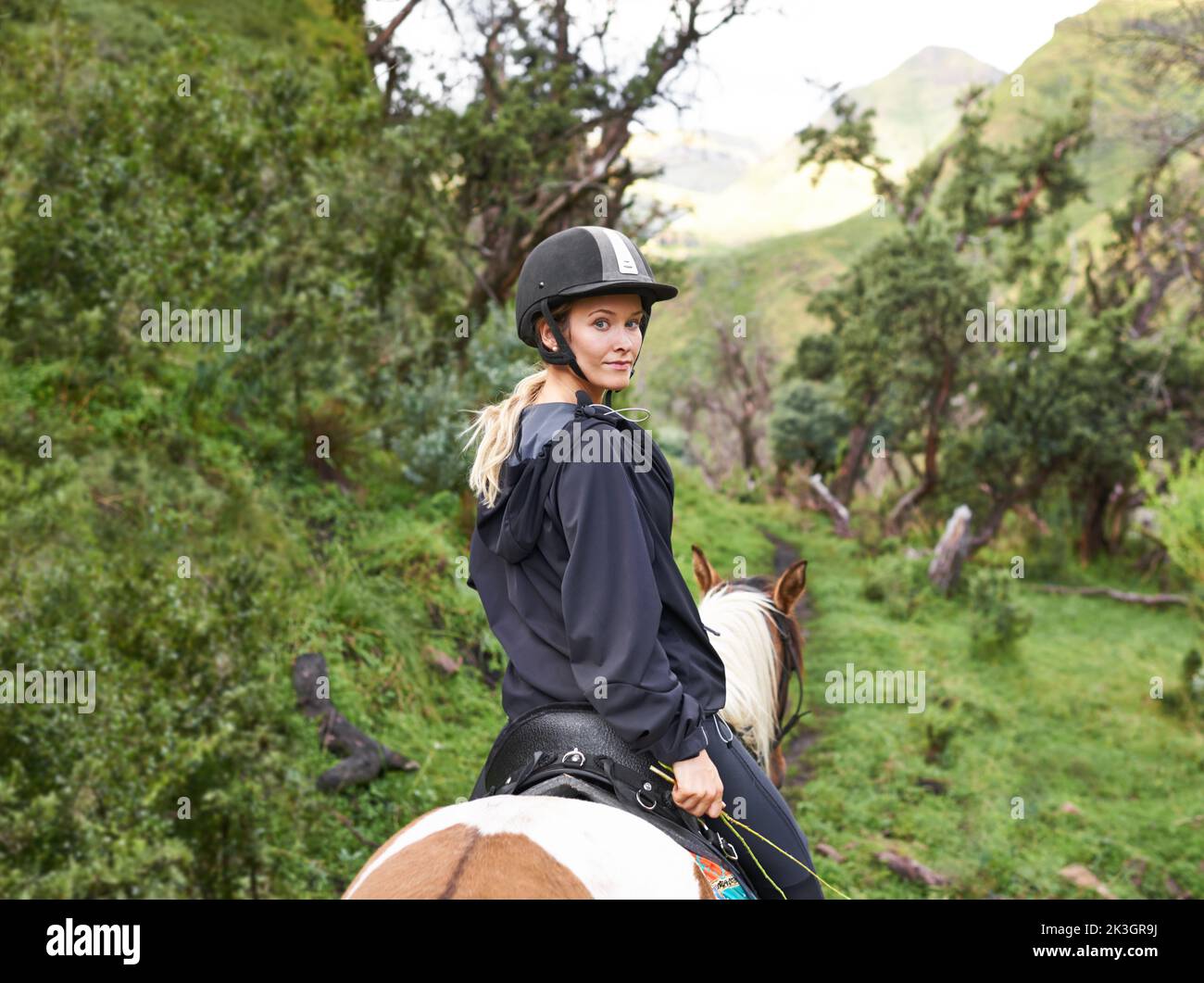 Équitation dans l'Outback. Une jeune femme attirante qui fait une balade à cheval sur un sentier de montagne. Banque D'Images