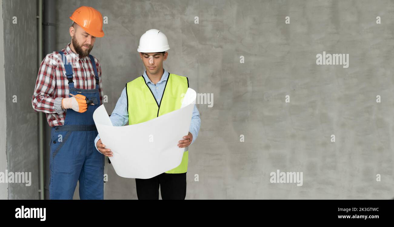 plans de discussion et plans de projet de l'architecte et de l'ingénieur en construction ou de l'arpenteur. Deux hommes portent des casques et sont debout sur la construction assis Banque D'Images
