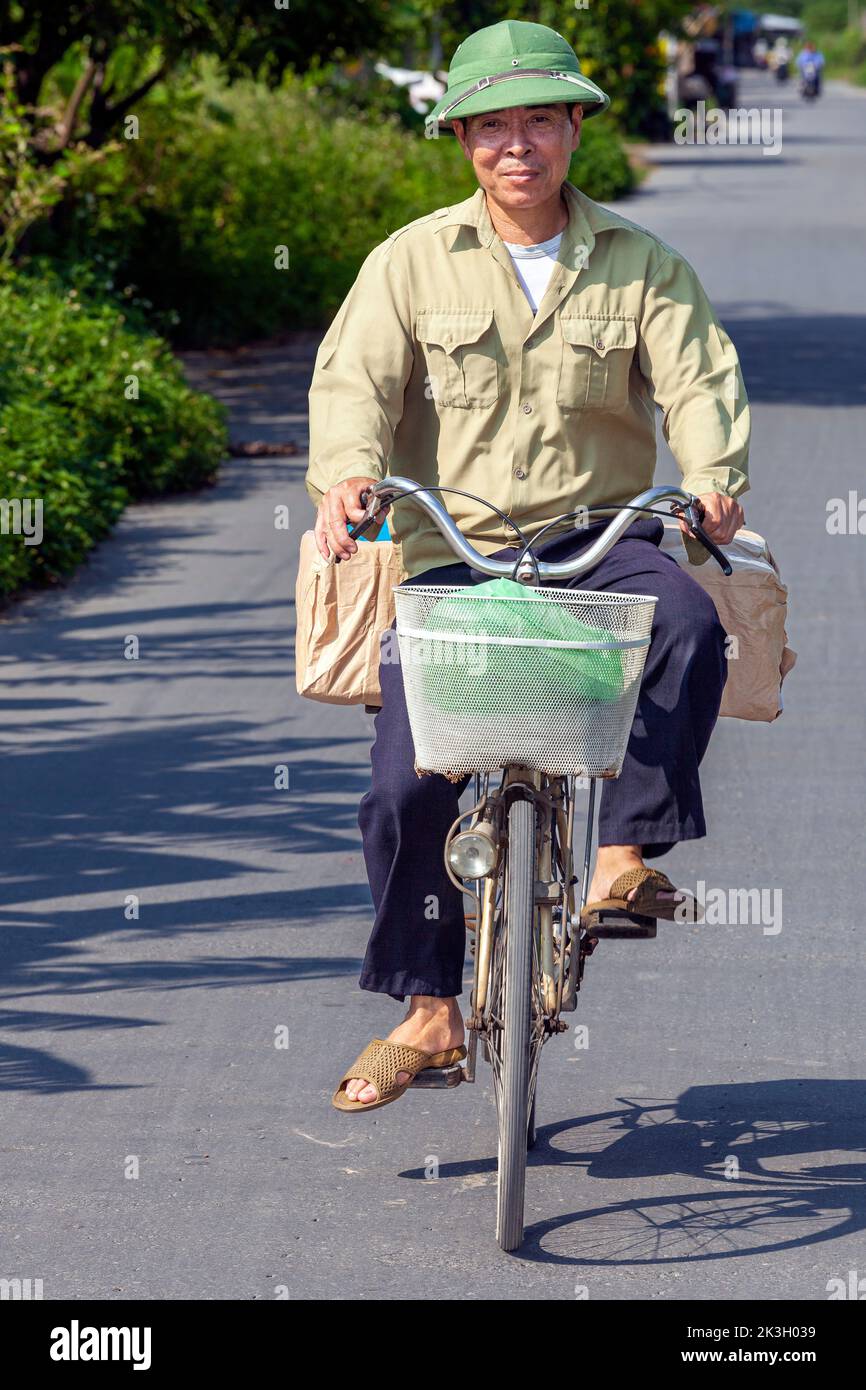 Cycliste portant un chapeau de bambou sur la route de campagne, Hai Phong rural, Vietnam Banque D'Images