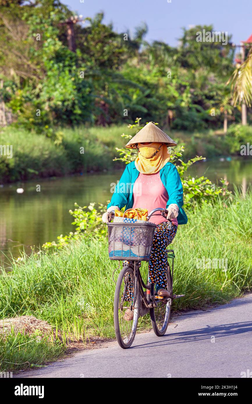 Cycliste portant un chapeau de bambou sur la route de campagne, Hai Phong rural, Vietnam Banque D'Images