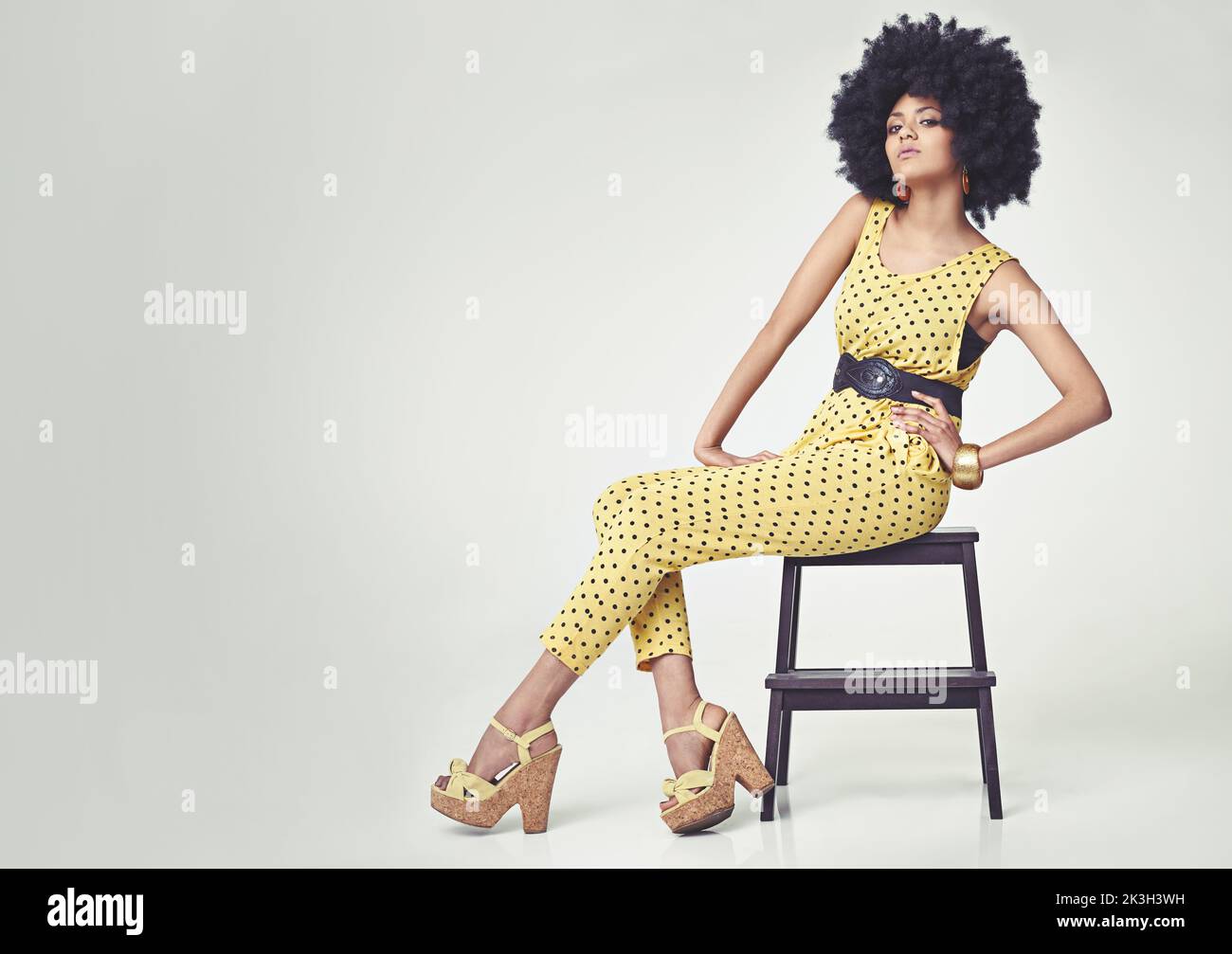 Un chic funky. Une jeune femme portant une combinaison rétro 70s tout en étant assise sur un tabouret dans le studio. Banque D'Images