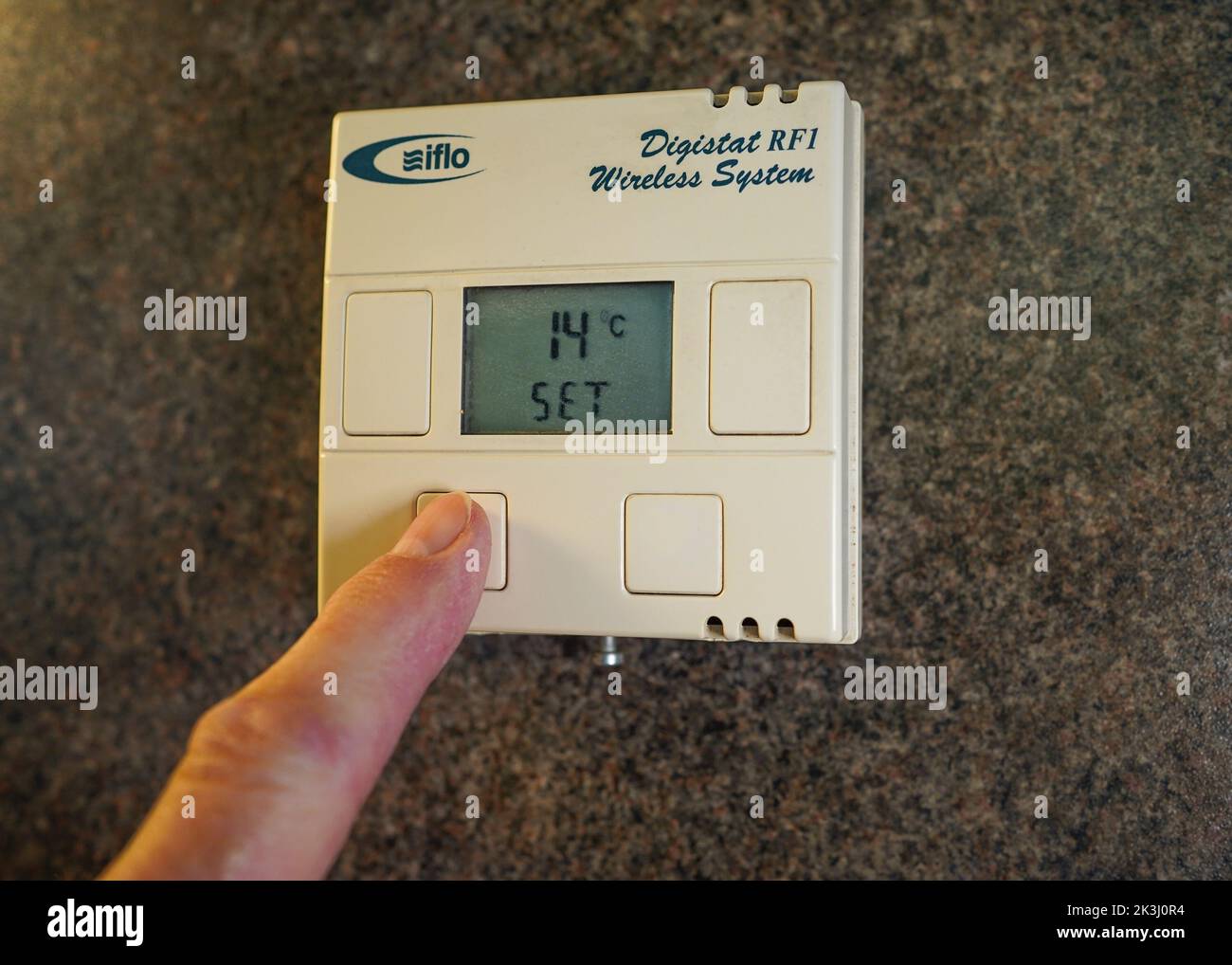Gros plan sur le thermostat de la salle de pression des doigts qui permet de régler le contrôle du chauffage à un niveau bas en raison de la crise énergétique du coût de la vie au Royaume-Uni. Banque D'Images