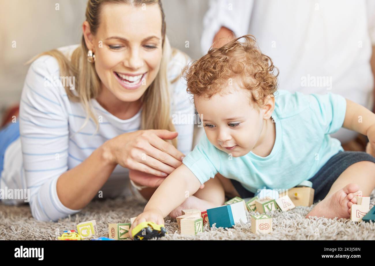 La mère, l'enfant et le jeu bloc d'apprentissage jouets sur le sol pour le collage éducatif temps ensemble dans la maison de famille. Jeune femme, bienveillante et aimante aidant le tout-petit Banque D'Images