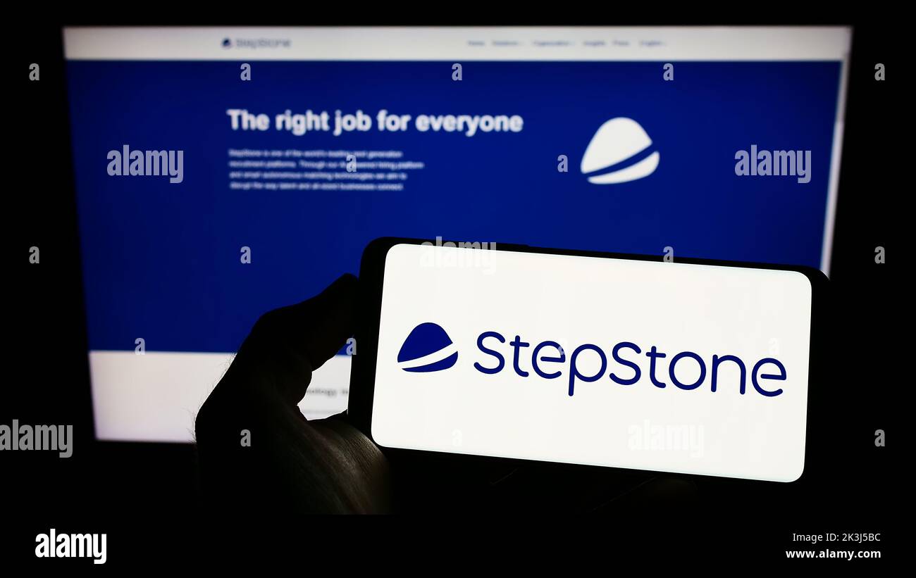 Personne tenant le téléphone portable avec le logo de la société allemande de conseil d'emploi StepStone GmbH sur l'écran en face de la page web d'affaires. Mise au point sur l'affichage du téléphone. Banque D'Images