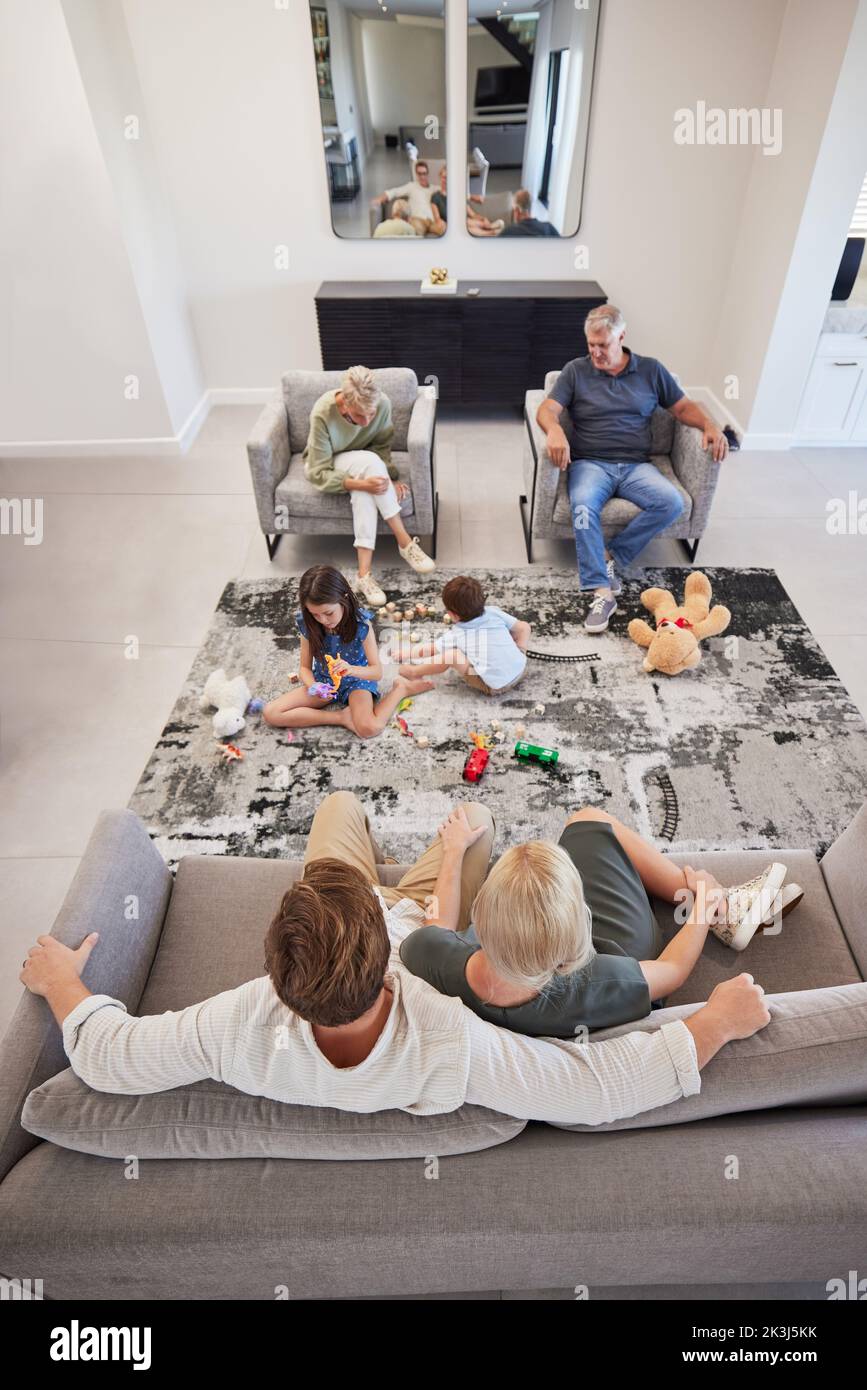 Famille, détente et enfants jouant avec des jouets sur le sol dans la salle de séjour tout en se liant. Calme grands-parents et parents se reposant tout en regardant le Banque D'Images
