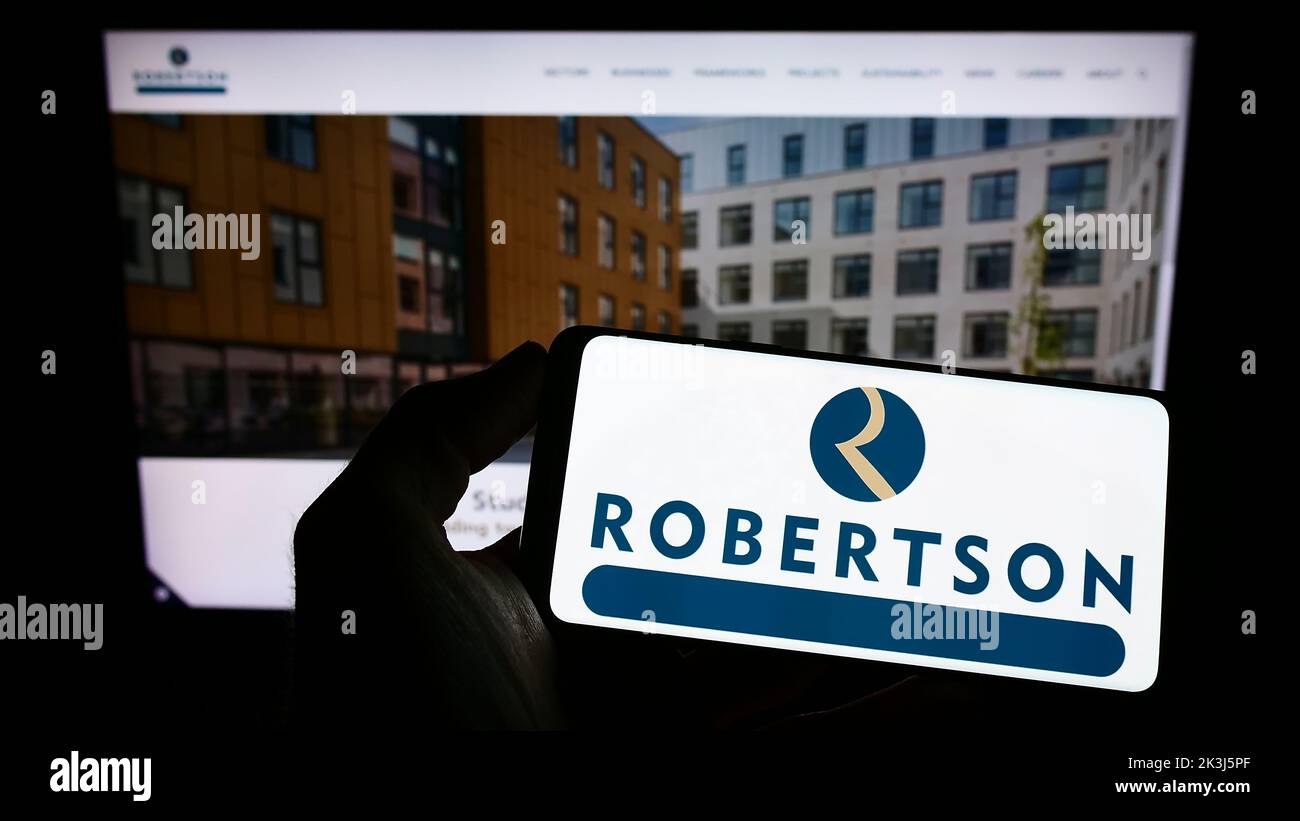 Personne tenant un téléphone portable avec le logo de la société de construction Robertson Group Limited à l'écran en face de la page Web. Mise au point sur l'affichage du téléphone. Banque D'Images