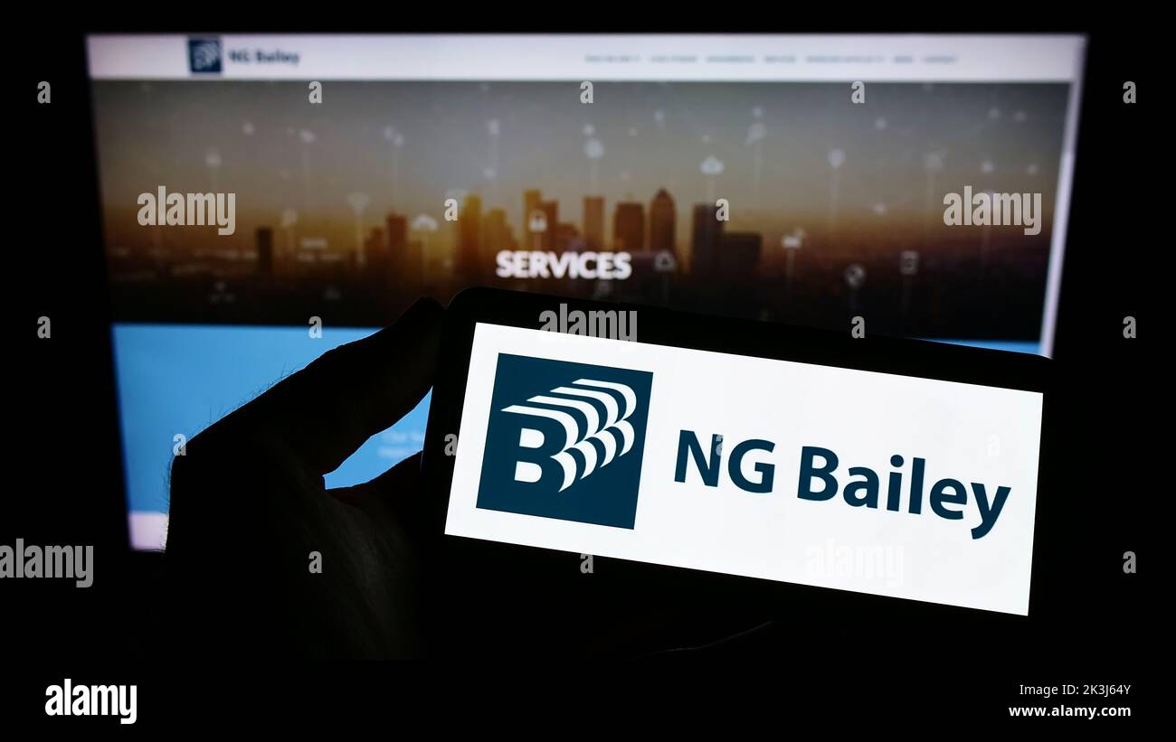 Personne tenant un téléphone portable avec le logo de la société d'ingénierie NG Bailey Group Limited à l'écran en face de la page Web. Mise au point sur l'affichage du téléphone. Banque D'Images
