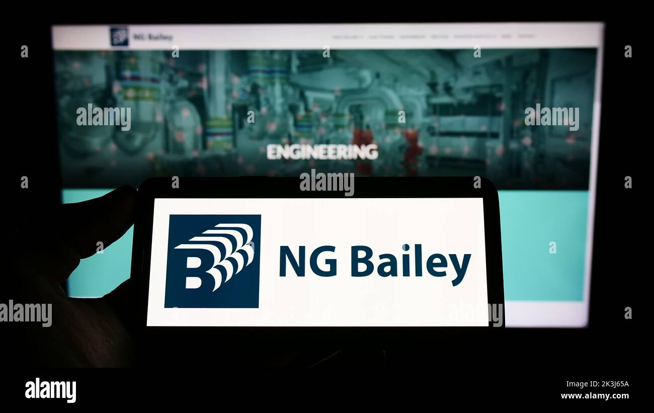 Personne tenant un téléphone portable avec le logo de la société d'ingénierie NG Bailey Group Limited à l'écran en face de la page Web d'affaires. Mise au point sur l'affichage du téléphone. Banque D'Images