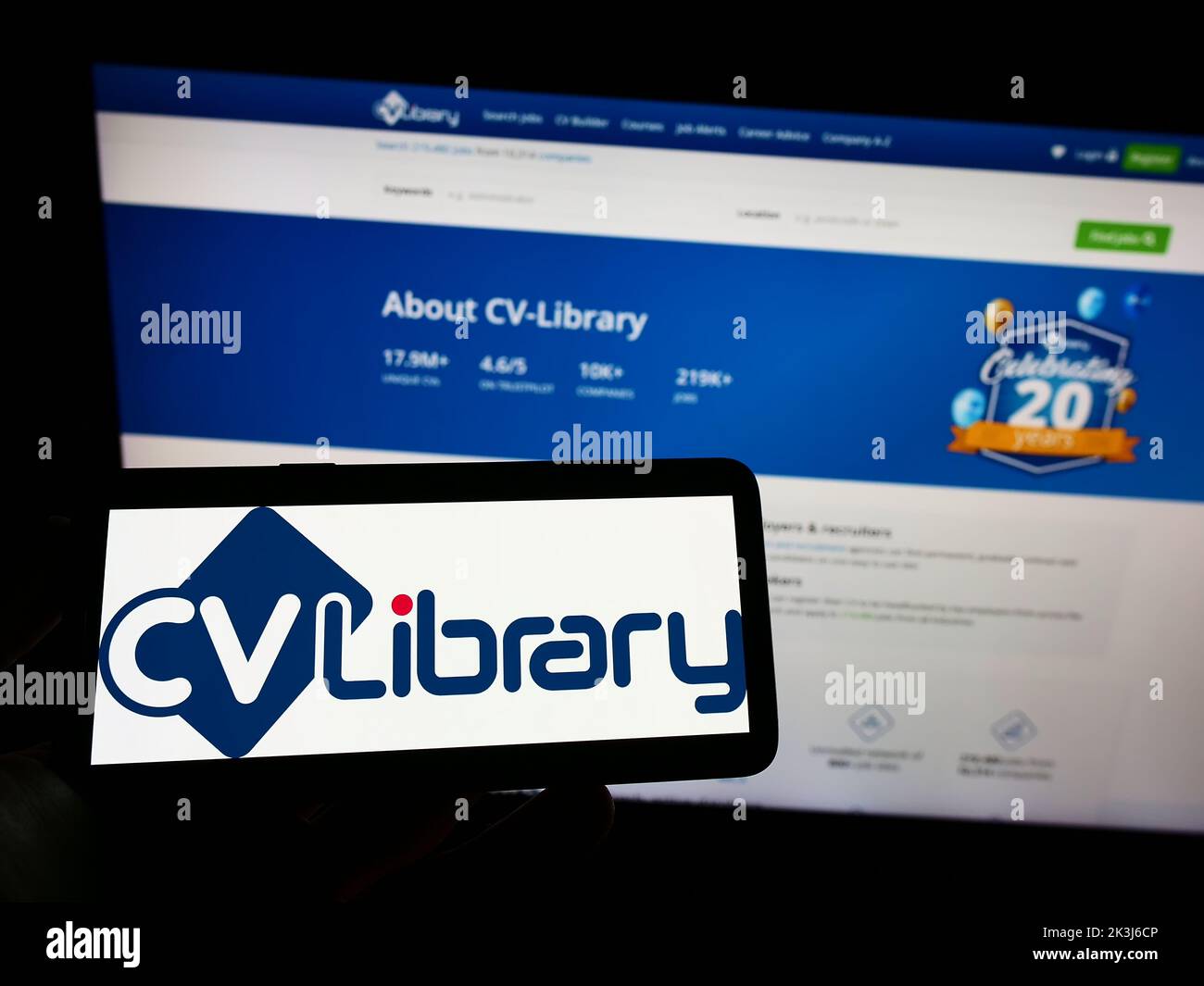Personne tenant un téléphone portable avec le logo de la société britannique de conseil d'emploi CV-Library Ltd. À l'écran devant la page Web d'affaires. Mise au point sur l'affichage du téléphone. Banque D'Images