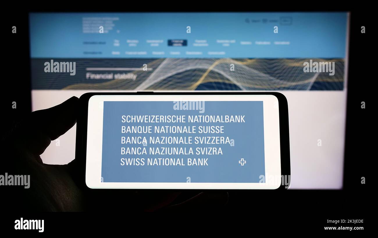 Personne titulaire d'un téléphone portable avec logo de l'institution financière Banque nationale suisse (BNS) à l'écran devant la page web. Mise au point sur l'affichage du téléphone. Banque D'Images