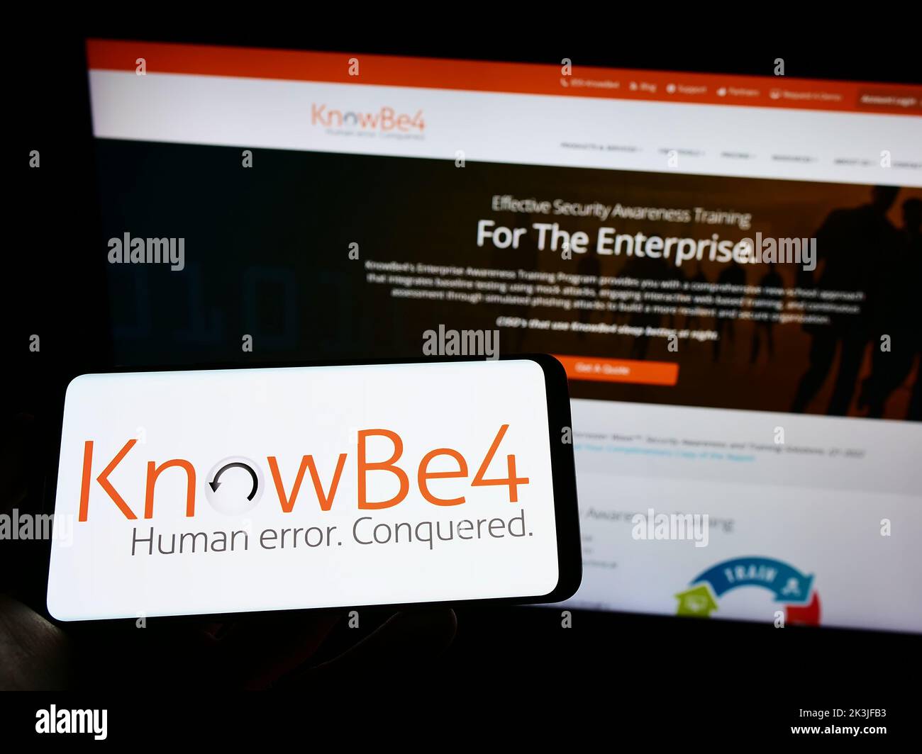 Personne portant un smartphone portant le logo de la société américaine de sensibilisation à la sécurité KnowBe4 Inc. À l'écran devant le site Web. Mise au point sur l'affichage du téléphone. Banque D'Images