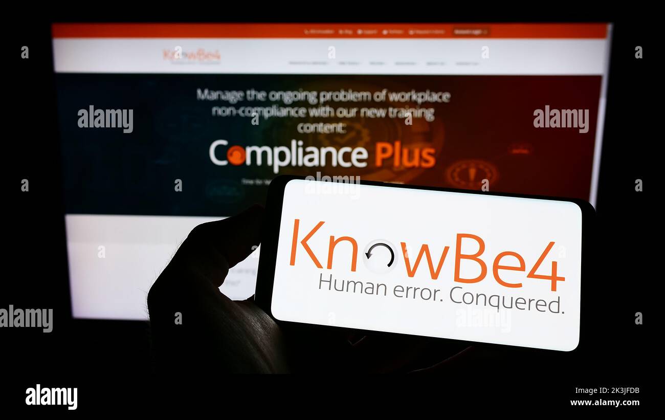 Personne tenant un téléphone portable avec le logo de la société américaine de sensibilisation à la sécurité KnowBe4 Inc. À l'écran en face de la page Web d'affaires. Mise au point sur l'affichage du téléphone. Banque D'Images