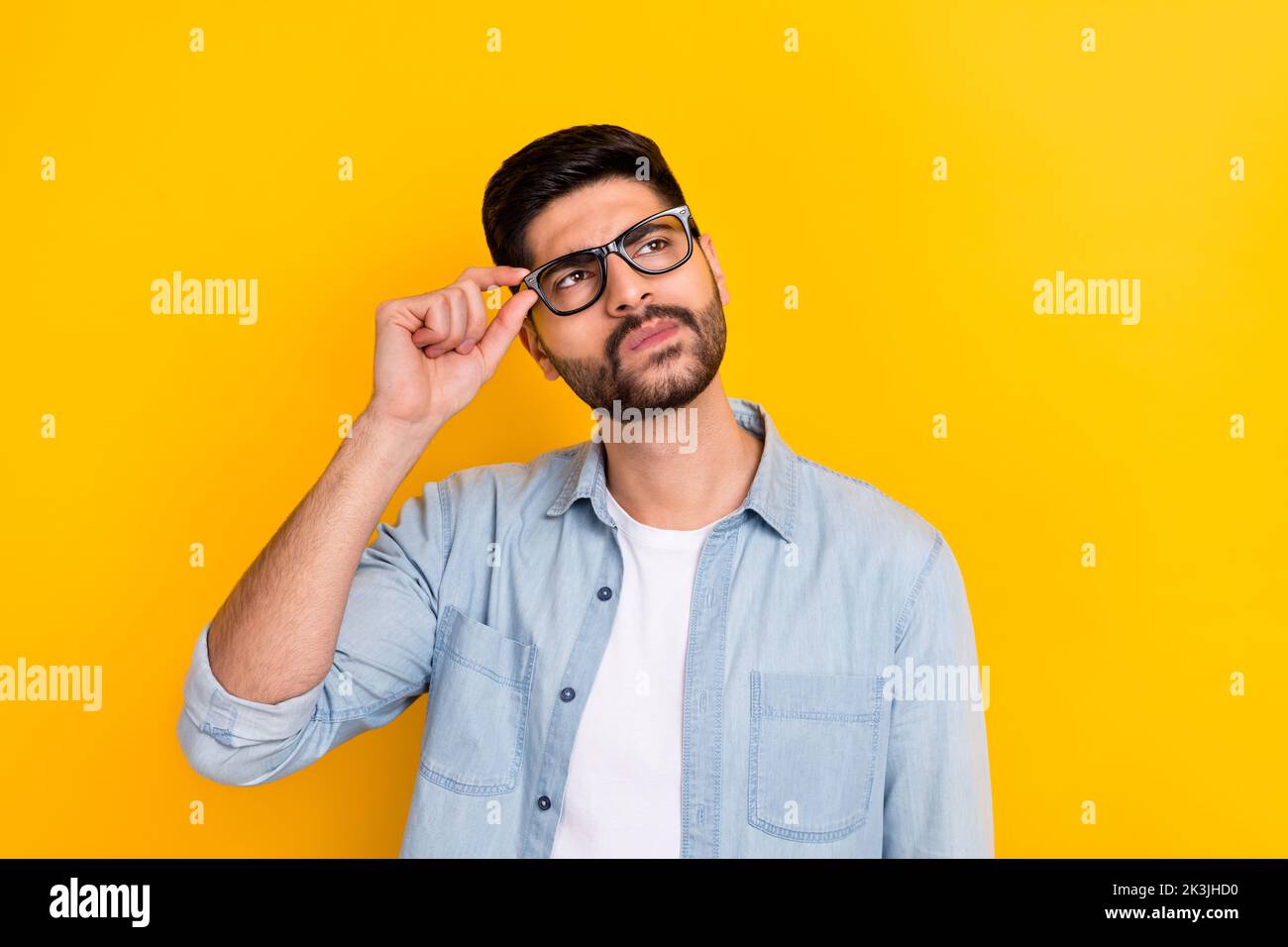 Portrait d'un jeune homme d'affaires réfléchi en lunettes rêvant sérieusement sur fond jaune vif Banque D'Images