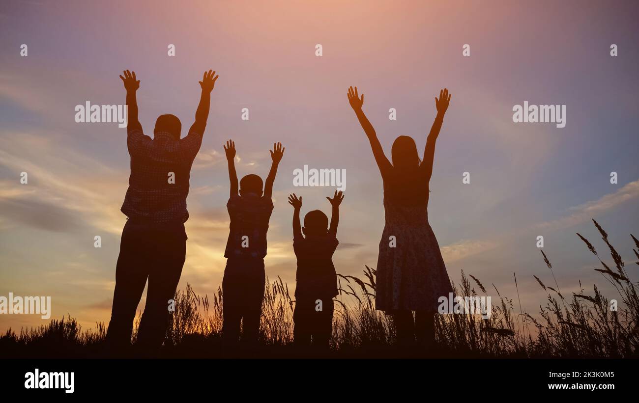 Les silhouettes des parents et des enfants élèvent les mains jusqu'au ciel au coucher du soleil Banque D'Images