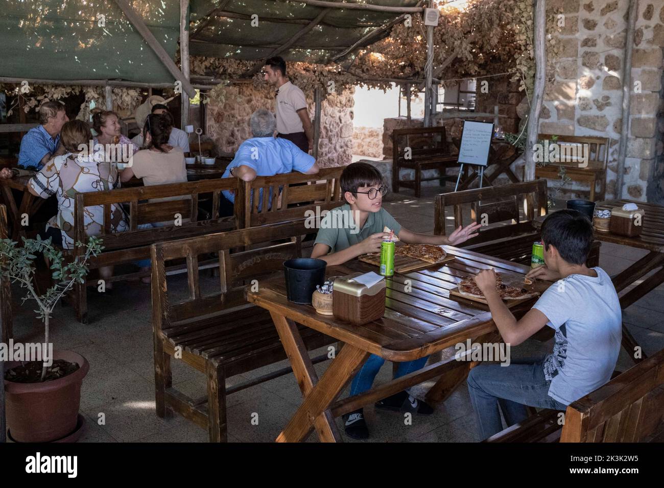 Les enfants avec leurs familles dîneront au Kafro's Pizza, Mardin. Il y a une pizzeria appelée Kafro's Pizza dans le village d'Elbegendi dans le quartier Midyat de Mardin. La pizzeria tire son nom du village d'Elbegendi, où vivent les Assyriens, sur le mont Bagok. La pizzeria, dont le propriétaire et le personnel sont Assyriens, accueille des dizaines de clients chaque jour en raison de son emplacement dans le village et de ses délicieuses pizzas. Nail Demir, le propriétaire du lieu, a appris à faire de la pizza tout en vivant en Europe et a décidé d'ouvrir Kafro's Pizza il y a 10 ans dans le village où il est né. Banque D'Images