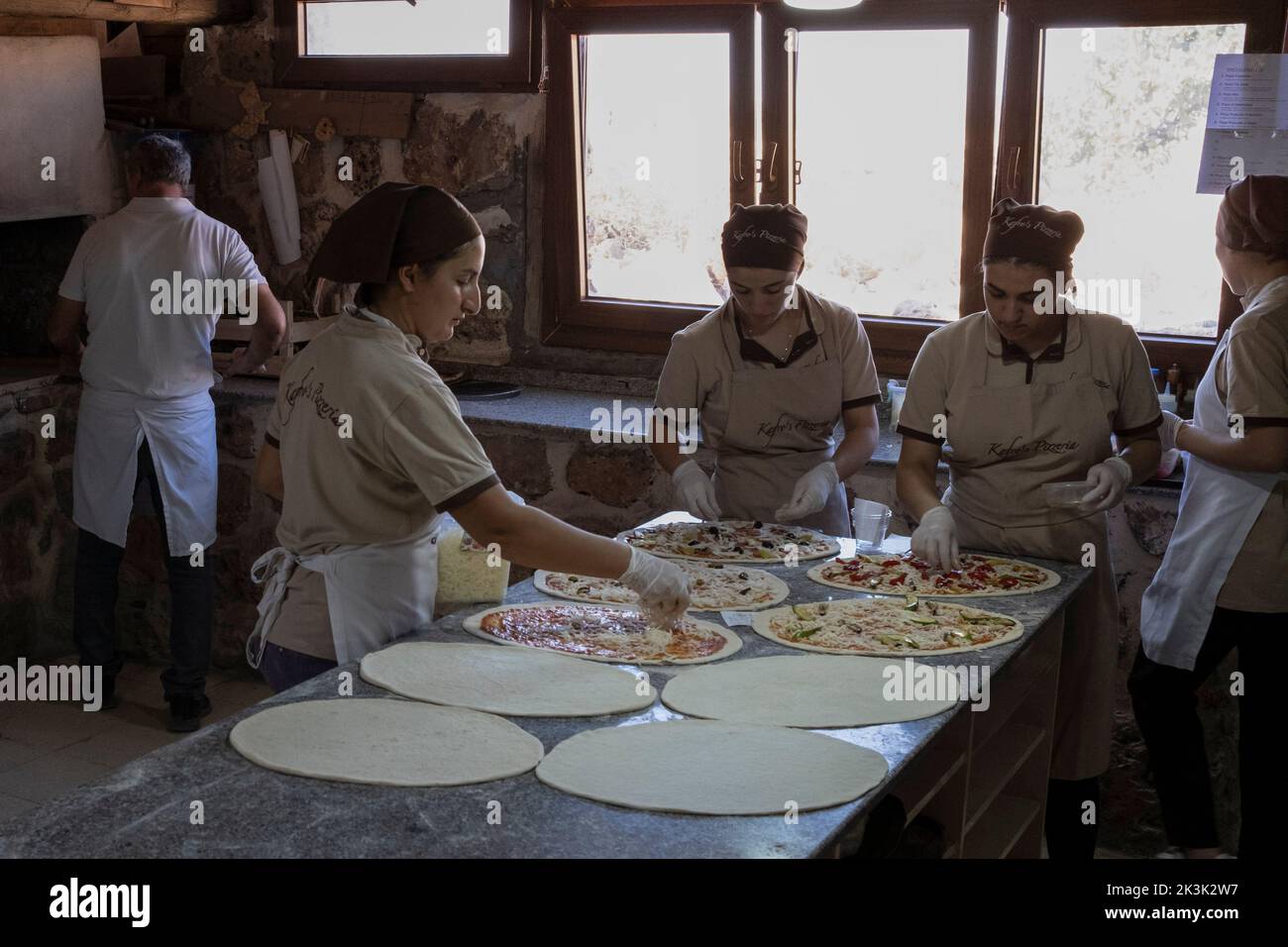 Des femmes assyriennes ont vu préparer des pizzas à Kafro's Pizza, Mardin. Il y a une pizzeria appelée Kafro's Pizza dans le village d'Elbegendi dans le quartier Midyat de Mardin. La pizzeria tire son nom du village d'Elbegendi, où vivent les Assyriens, sur le mont Bagok. La pizzeria, dont le propriétaire et le personnel sont Assyriens, accueille des dizaines de clients chaque jour en raison de son emplacement dans le village et de ses délicieuses pizzas. Nail Demir, le propriétaire du lieu, a appris à faire de la pizza tout en vivant en Europe et a décidé d'ouvrir Kafro's Pizza il y a 10 ans dans le village où il est né. Banque D'Images