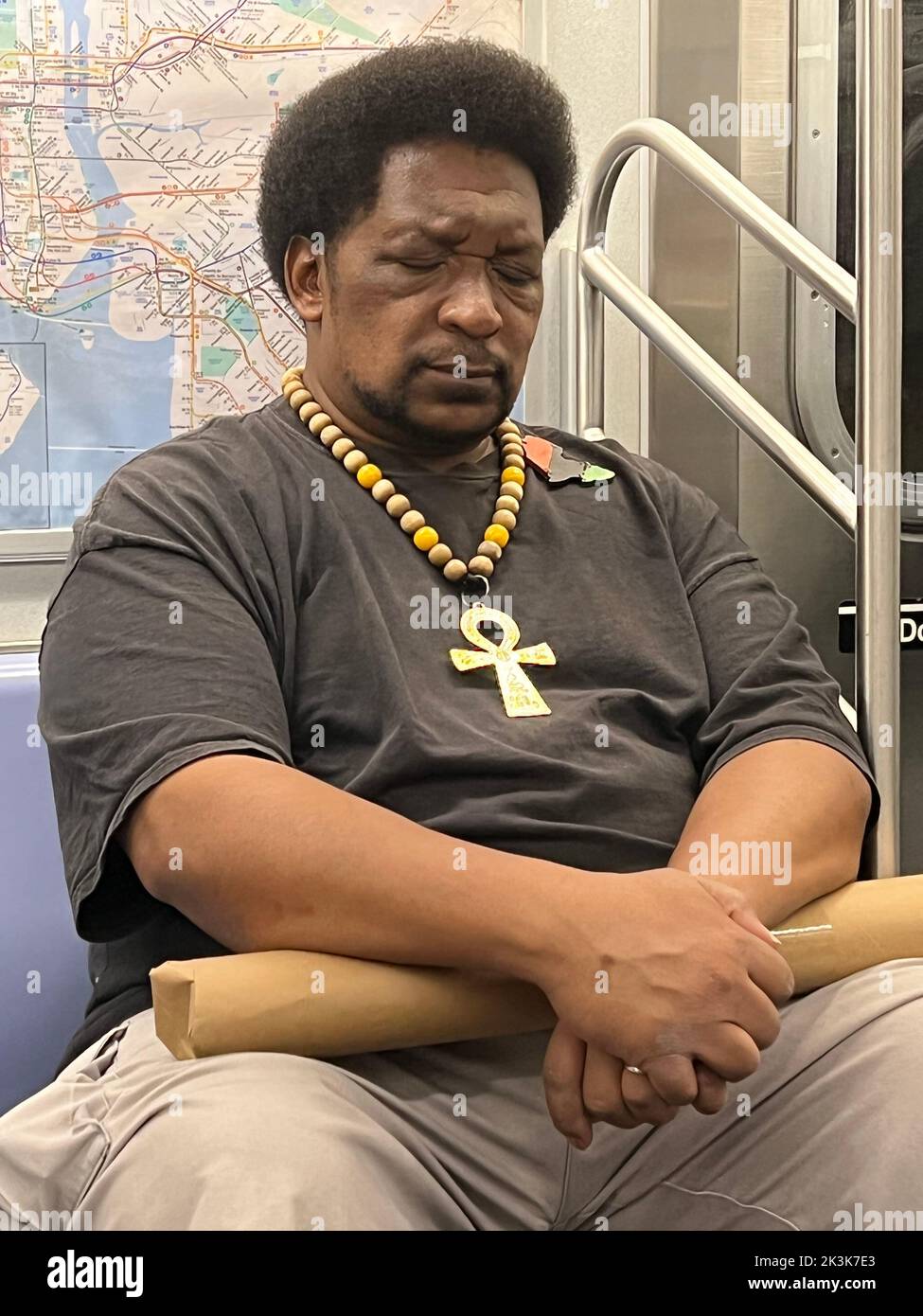 Homme portant un ankh (croix égyptienne) profondément dans la pensée sur un train de métro de New York. Banque D'Images