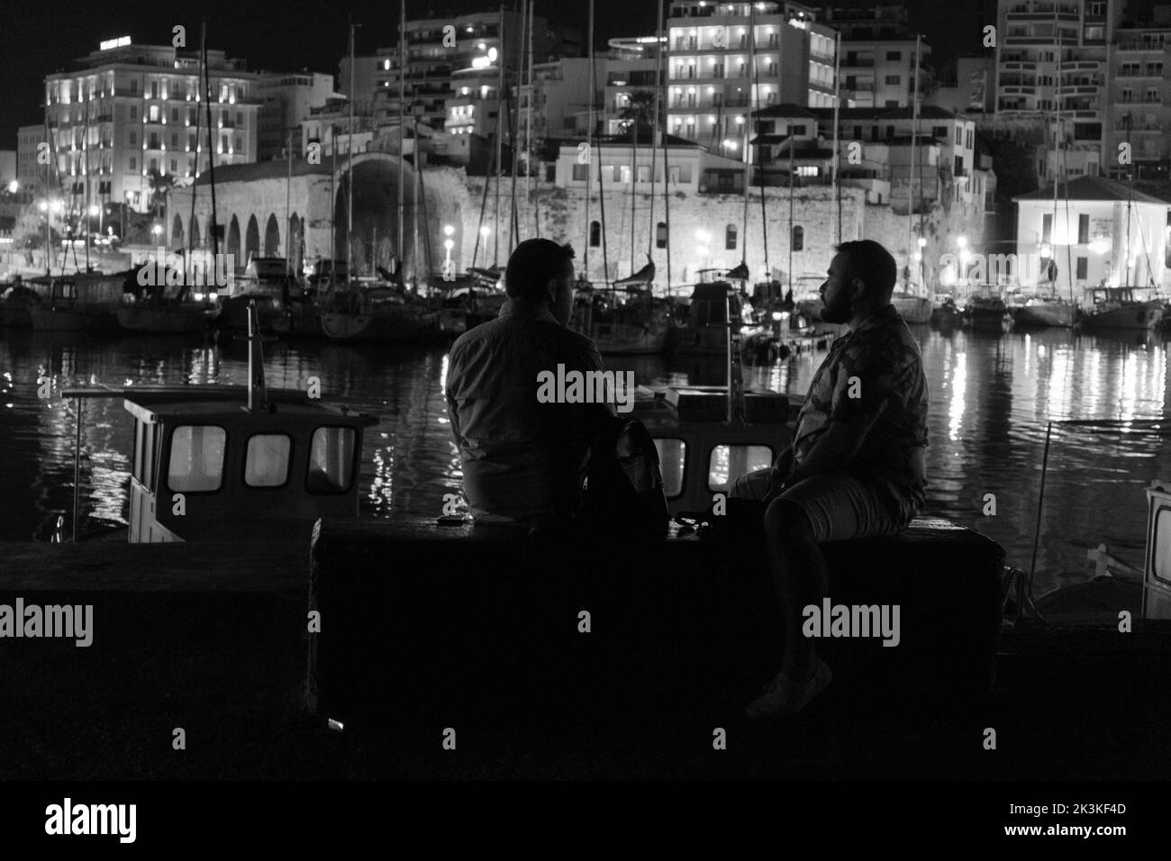 Héraklion, Grèce - 15 septembre 2022 : vue arrière de deux personnes parlant au milieu de la nuit en bord de mer assis sur un banc Banque D'Images