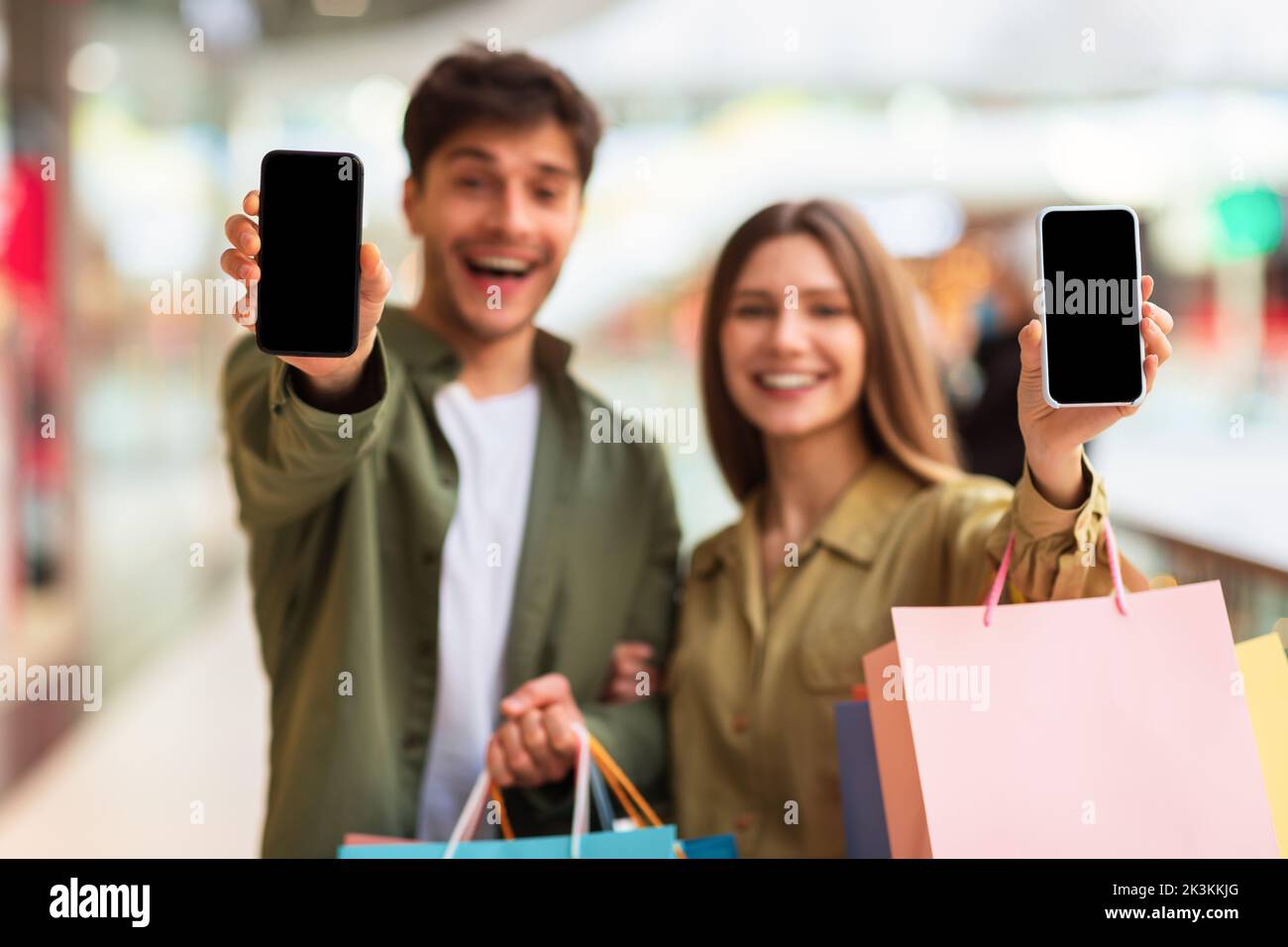 Les conjoints enthousiastes montrant des téléphones intelligents avec écran vide Shopping dans Mall Banque D'Images