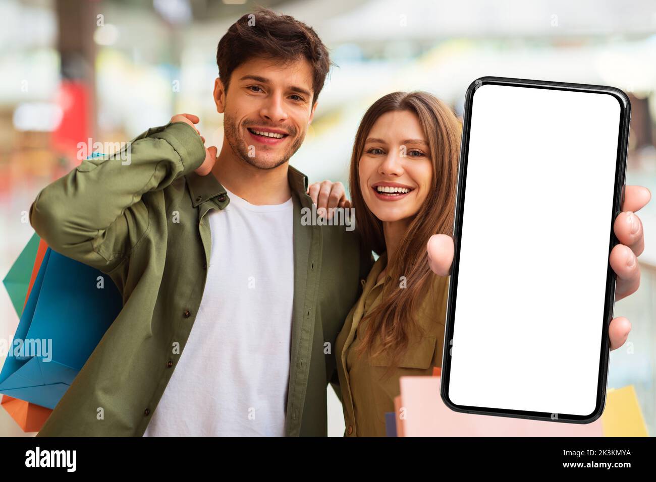 Couple joyeux montrant Big smartphone recommandant l'application Shopping dans Mall Banque D'Images