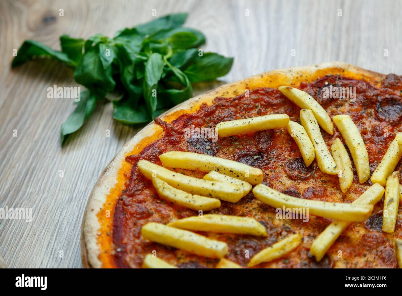Une savoureuse pizza Patatosa avec des saucisses chaudes et des frites dans une sauce tomate avec basilic à côté Banque D'Images