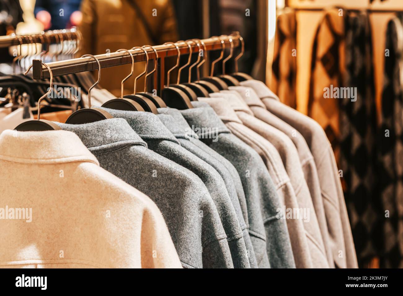 Manteaux élégants et décontractés suspendus sur un cintre dans un magasin de vêtements, intérieur flou de magasin Banque D'Images