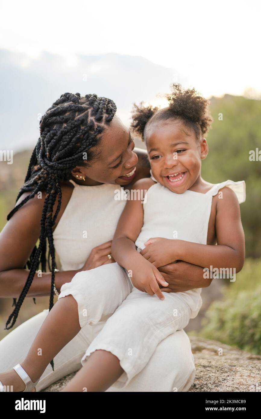 Merry African American mère avec des cheveux bouclés qui embrasse et chatouillent bonne fille tout en passant un week-end d'été dans la campagne ensemble Banque D'Images