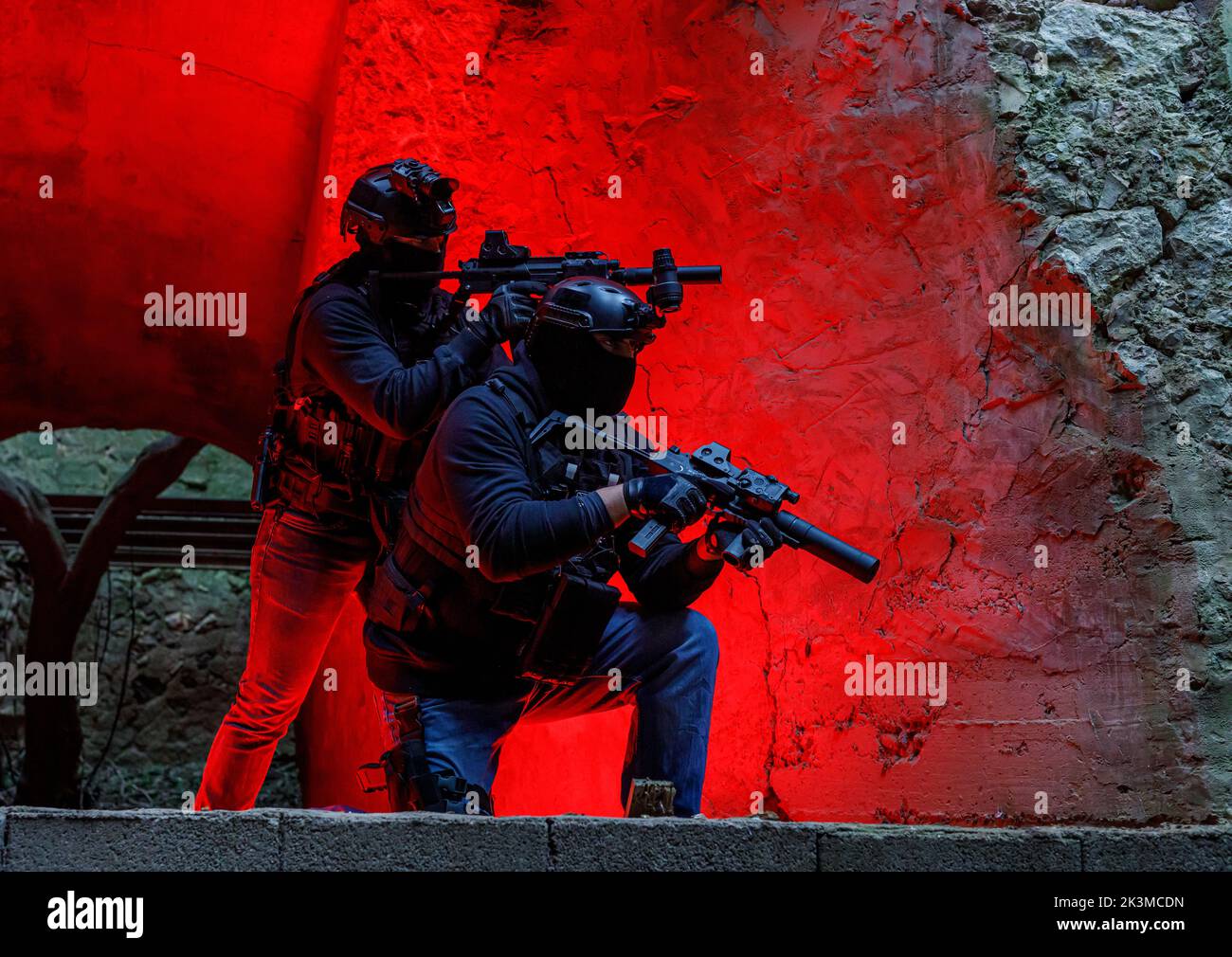 Vue latérale des combattants anonymes de l'équipe masculine en tenue de protection casques et masques avec fusils modernes dans la grotte rocheuse Banque D'Images