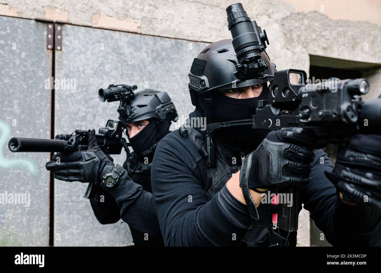 Corps complet de combattants des forces spéciales non reconnaissables en équipement de combat et casques de protection visant avec des fusils modernes près des murs du vieux bâtiment Banque D'Images