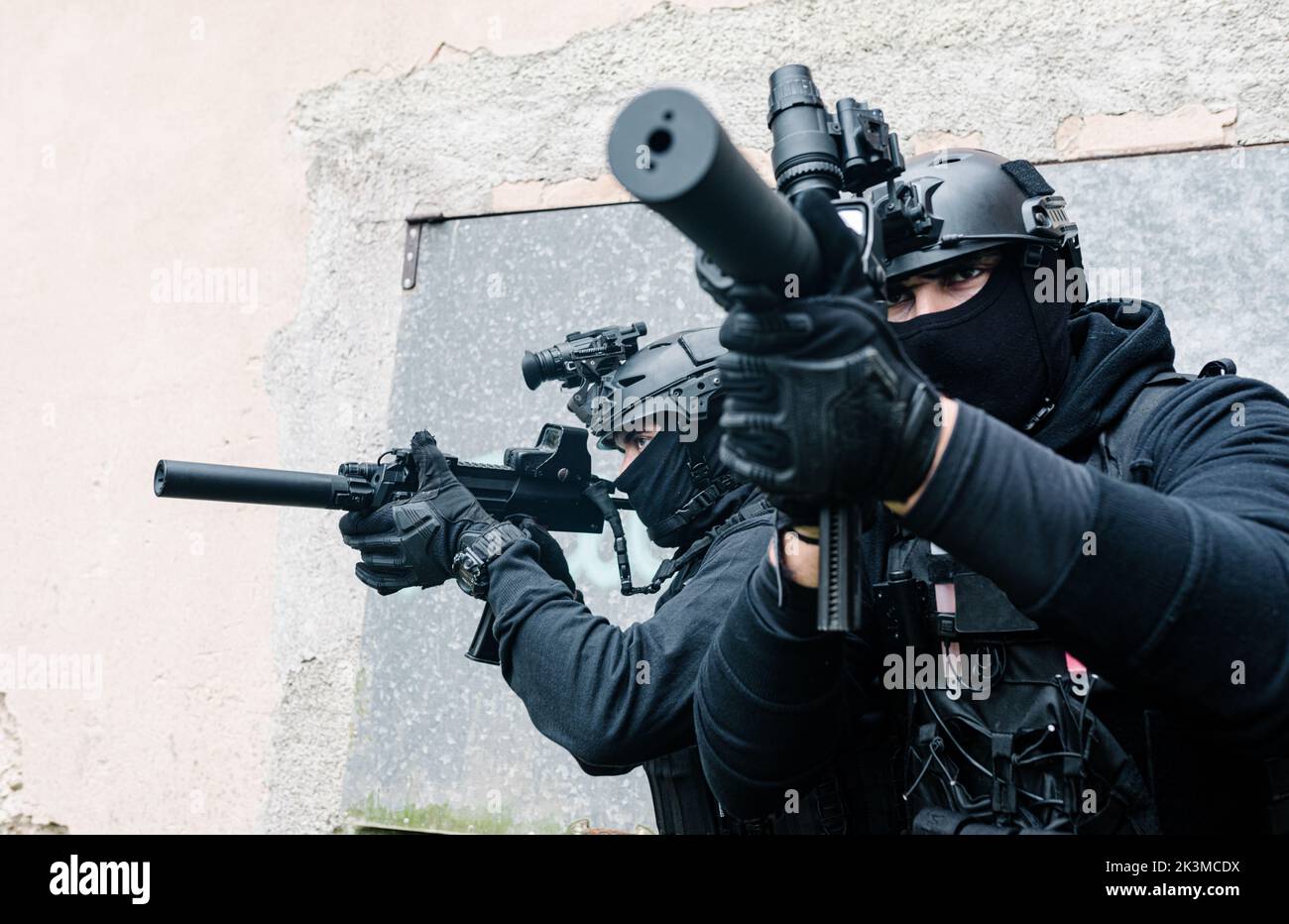 Corps complet de combattants des forces spéciales non reconnaissables en équipement de combat et casques de protection visant avec des fusils modernes près des murs du vieux bâtiment Banque D'Images