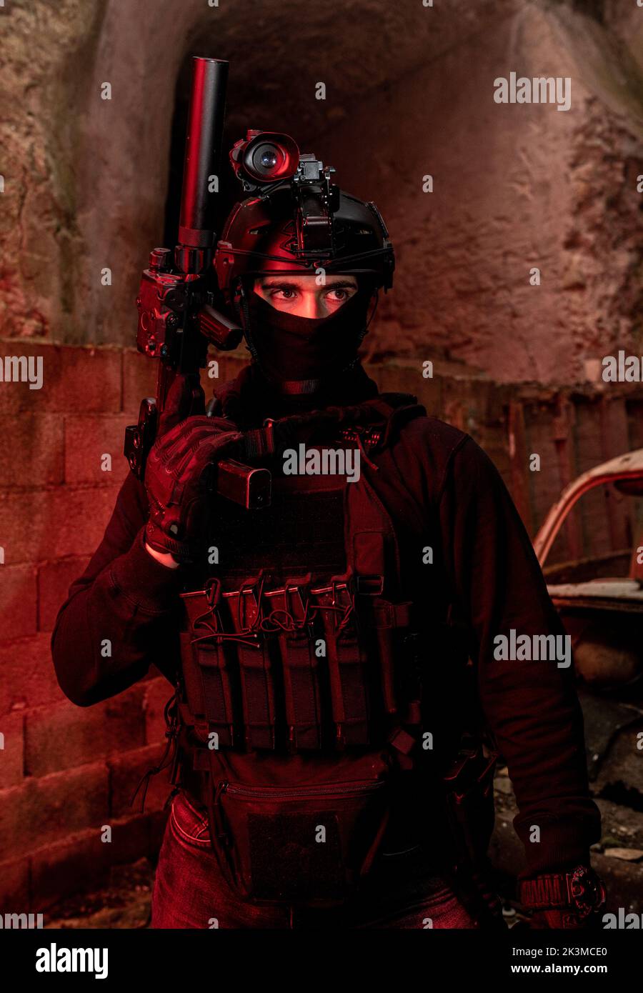Inreconnaissable, un jeune homme de combat attentif dans un équipement de combat et un casque de protection qui regarde loin dans une pièce lumineuse au néon Banque D'Images