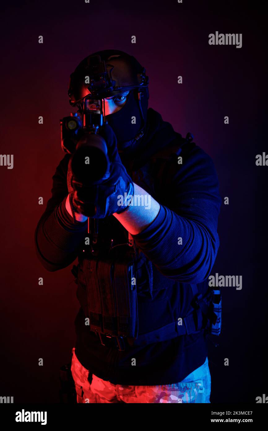 Méconnaissable un jeune homme attentif dans un équipement de combat et un casque de protection regardant la caméra à travers la lentille du fusil tout en prenant le but dans une pièce sombre Banque D'Images